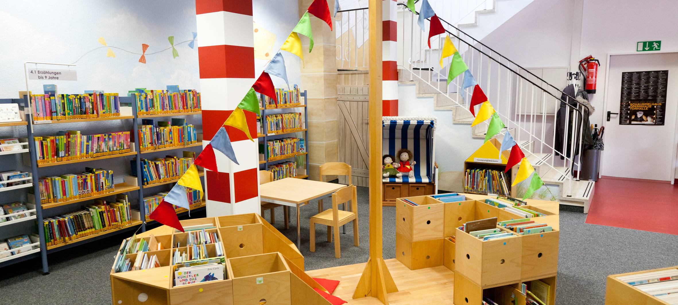 Ein Holzboot mit bunten Fahnen. Es steht in der Stadtbücherei in Eller am Gertrudisplatz.