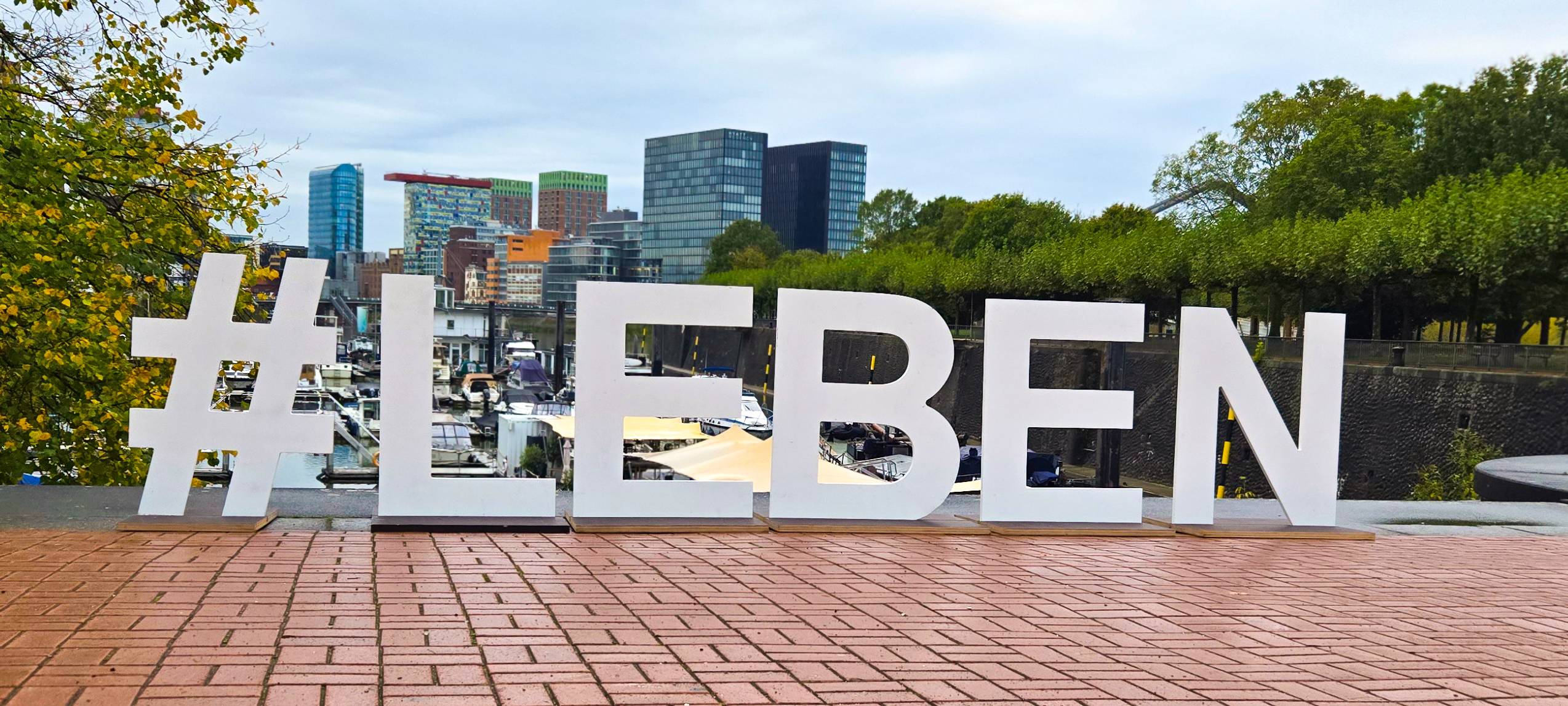 Ein großes Schild mit großen Buchstaben, das im Medienhafen aufgestellt ist. Zu lesen ist #LEBEN.