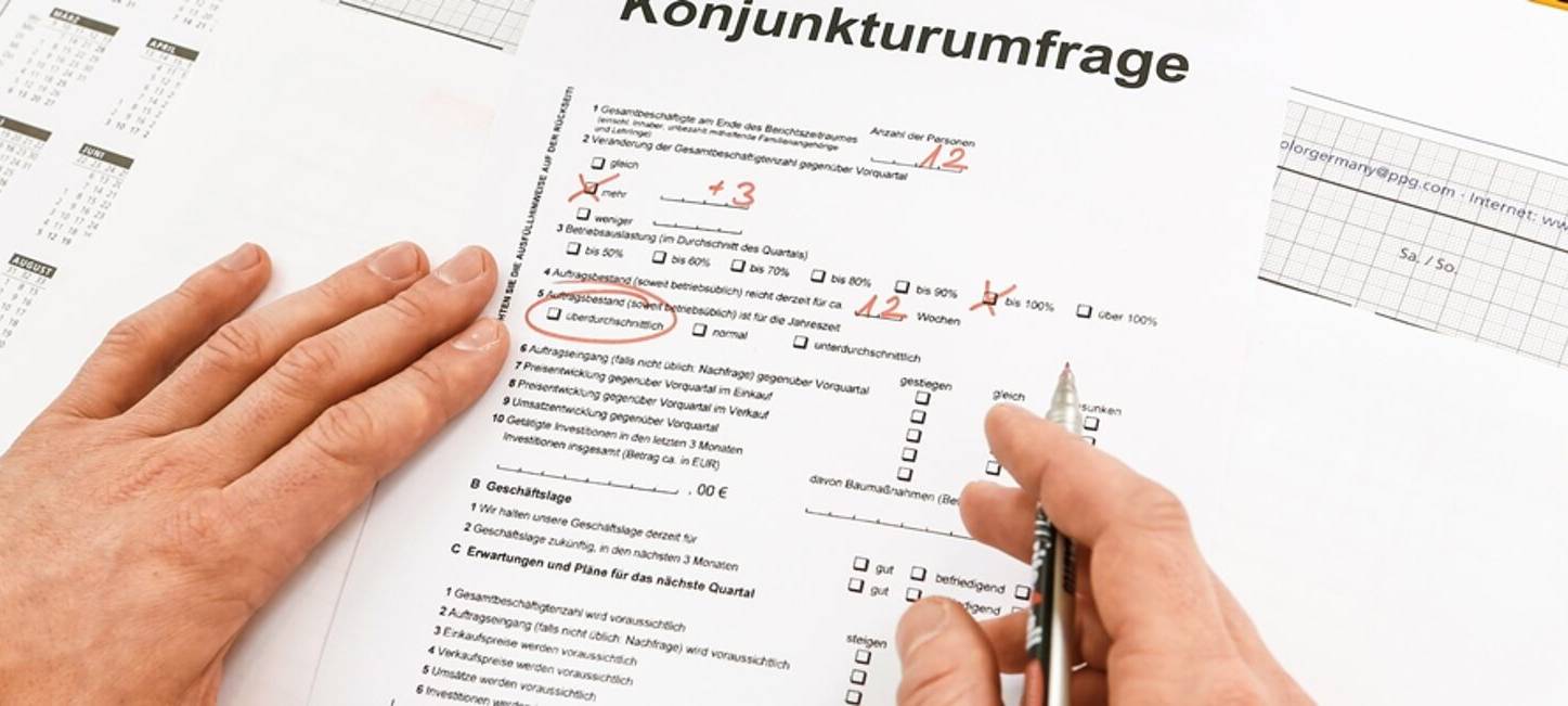 Eine Person füllt mit einem roten Kugelschreiber das Formular zur Konjunkturumfrage im Handwerk aus.