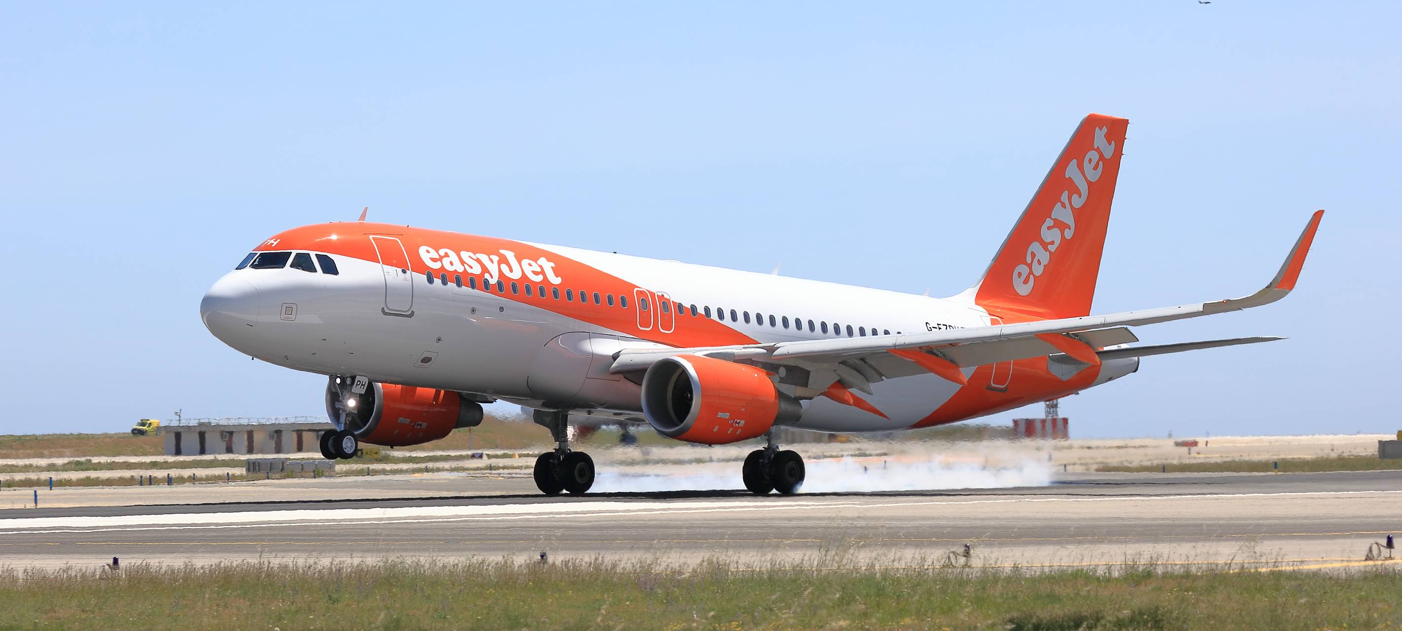 Ein rot-weißer Airbus 320 der Fluggesellschaft easyjet bei der Landung. Im Hintergrund das Gelände eines Flughafens.