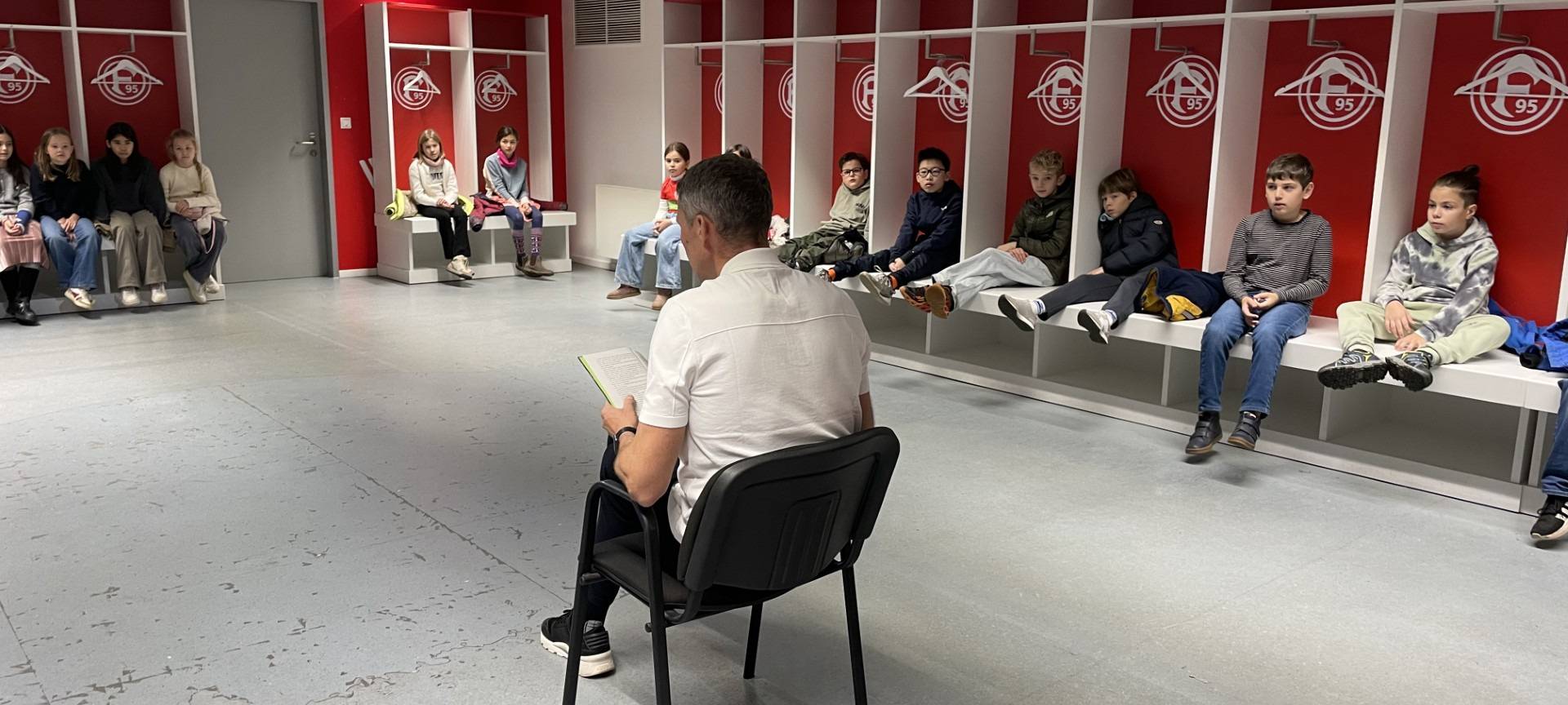 Fortuna-Legende Oliver Fink in der Heim-Kabine von Fortuna Düsseldorf. Er liest Kindern aus Niederkassel aus dem Buch "Woodwalkers" vor.