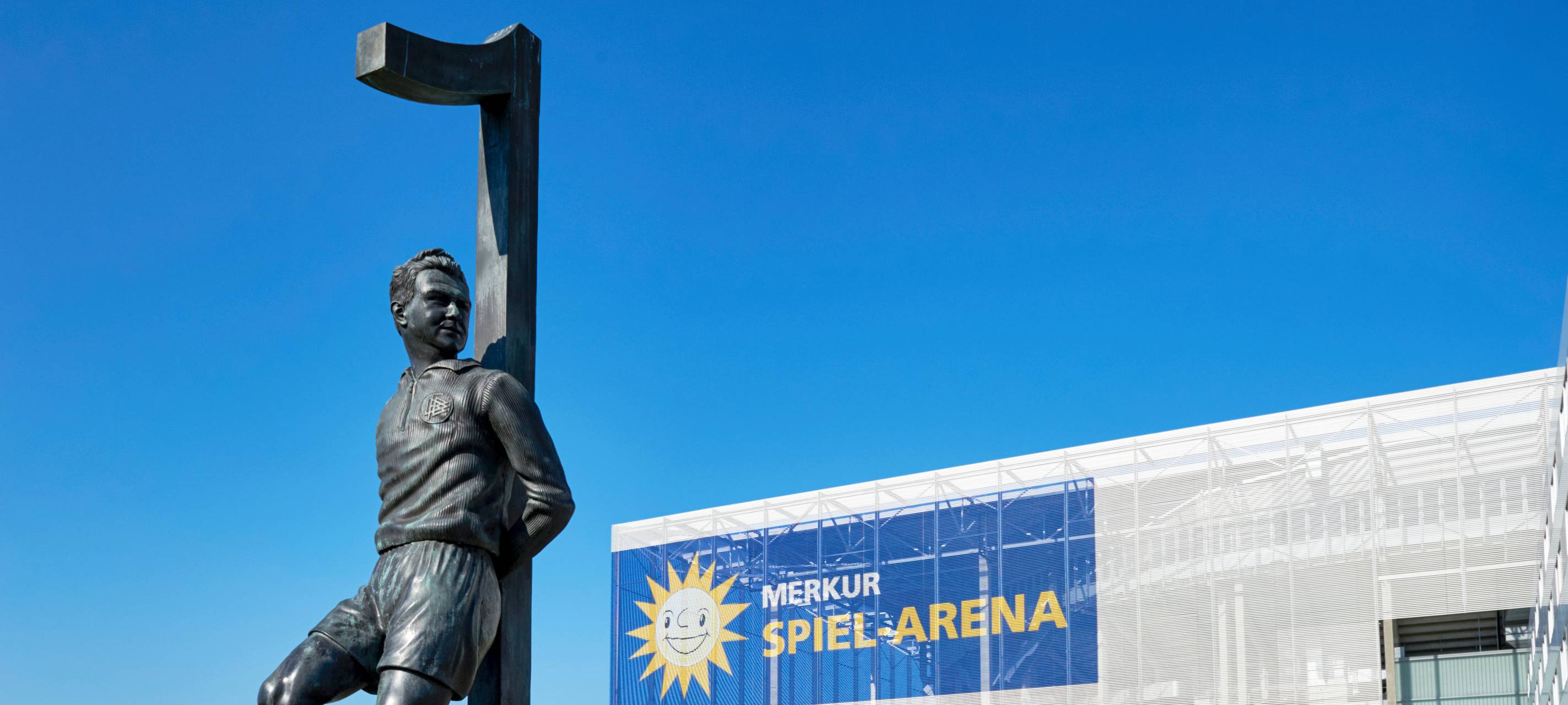 Die Merkur-Spiel-Arena im Hintergrund. Im Vordergrund steht das Toni-Turek-Denkmal auf dem Arena-Vorplatz.