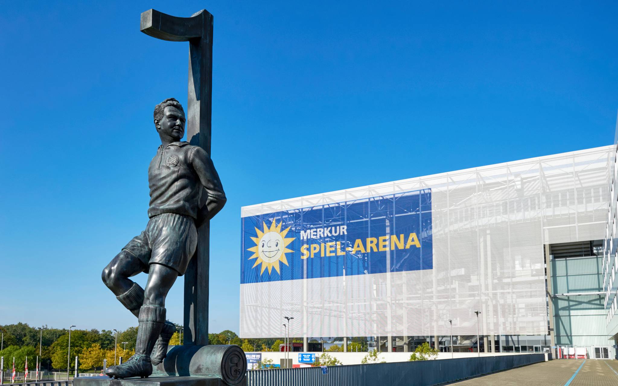 Die Merkur-Spiel-Arena im Hintergrund. Im Vordergrund steht das Toni-Turek-Denkmal auf dem Arena-Vorplatz.