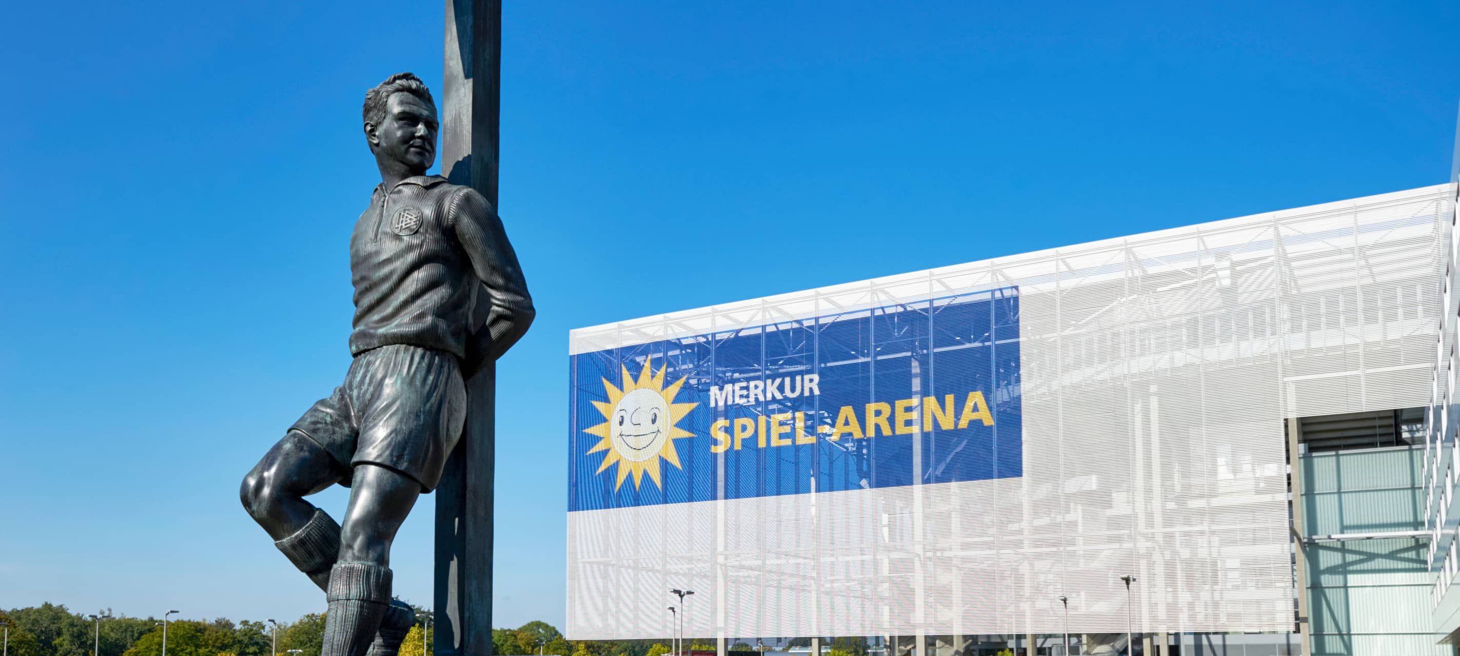 Die Merkur-Spiel-Arena im Hintergrund. Im Vordergrund steht das Toni-Turek-Denkmal auf dem Arena-Vorplatz.