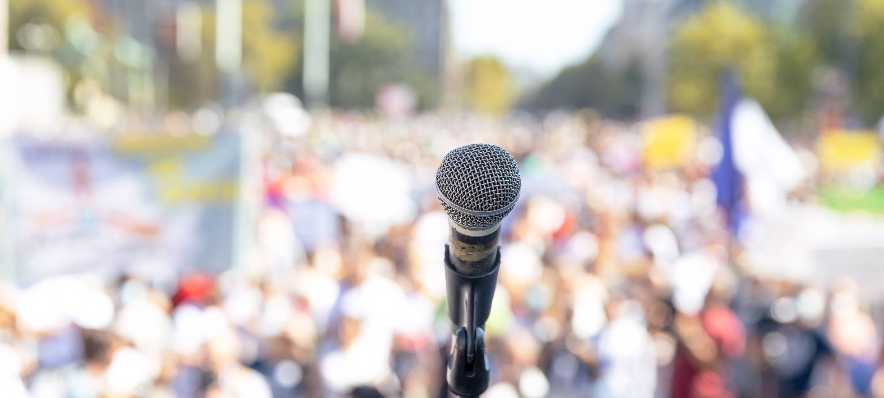 Ein Mikrofon vor einer Masse von Menschen. Die Menschen sind aber nur unscharf zu erkennen.