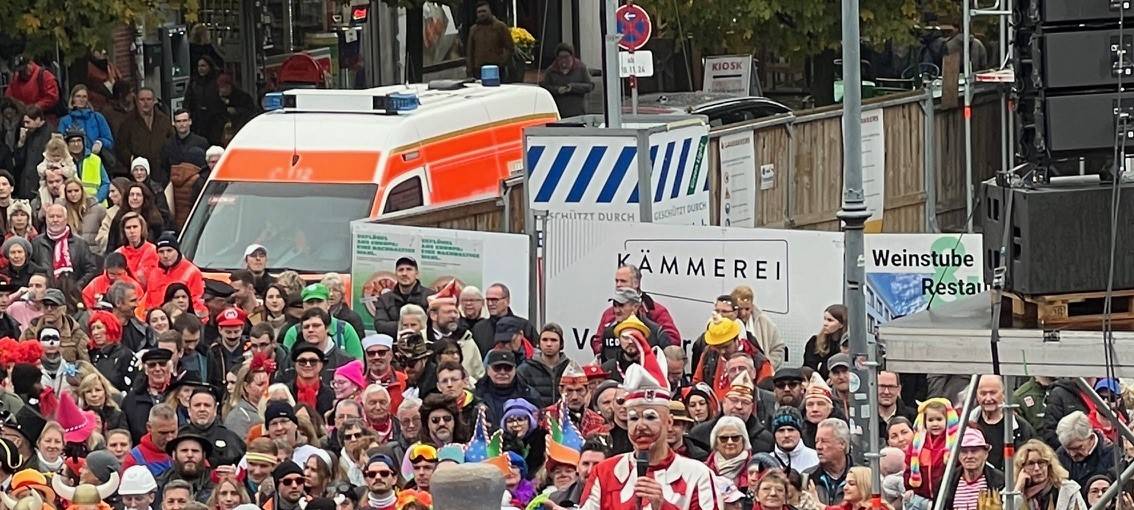 Der Hoppeditz hält seine Rede in einem Senftopf. Karnevalisten auf dem Marktplatz hören ihm zu.