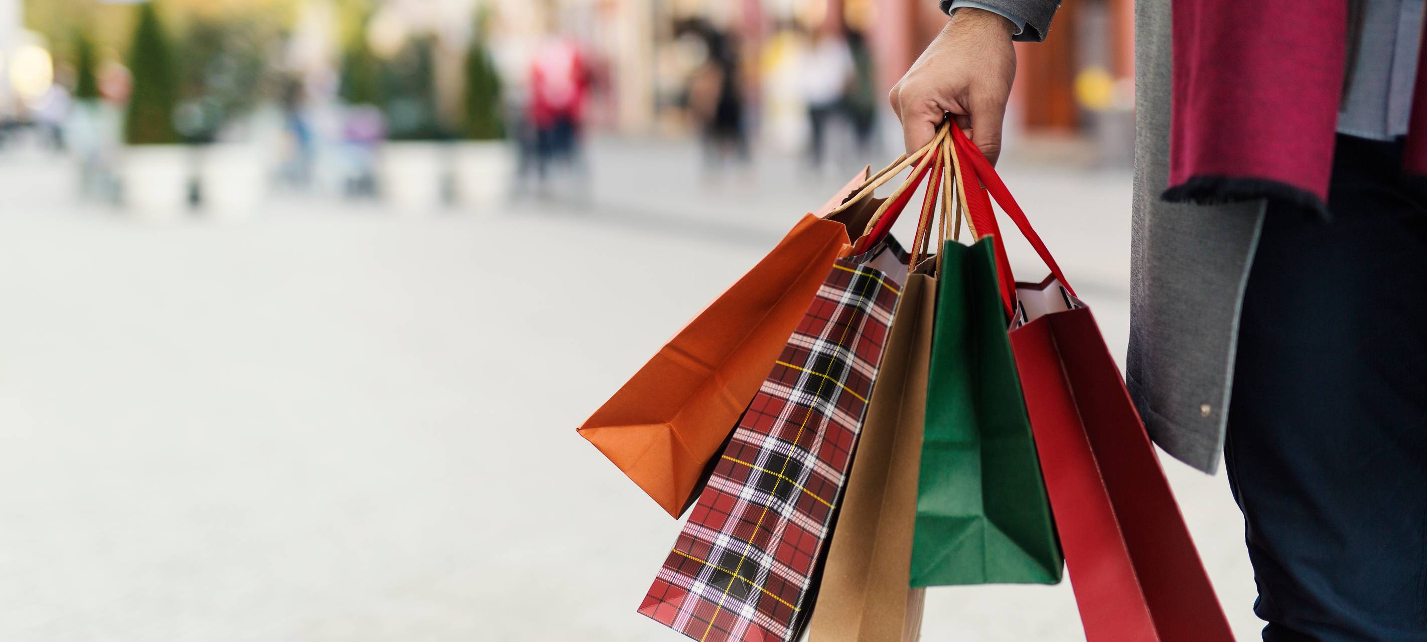 Verkaufsoffene Sonntage laden zum Shoppen ein. Ein unbekannter Mann hält vier unterschiedlich große Einkaufstüten in der Hand.