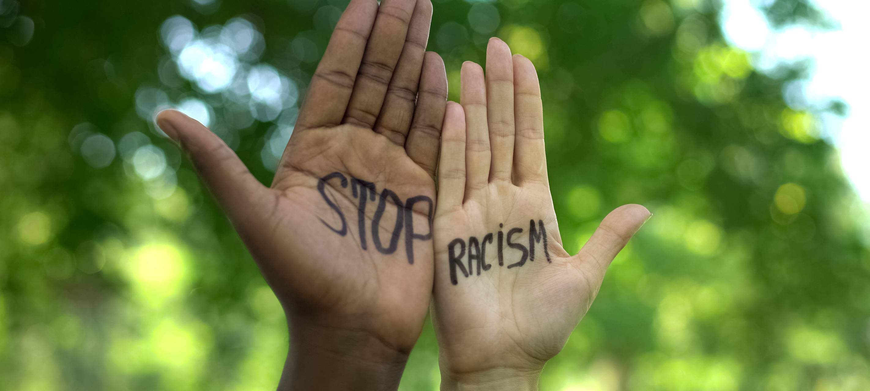 Zwei Hände werden in die Höhe gestreckt. Auf der linken Hand steht "Stop" und auf der rechten Hand "Racism".