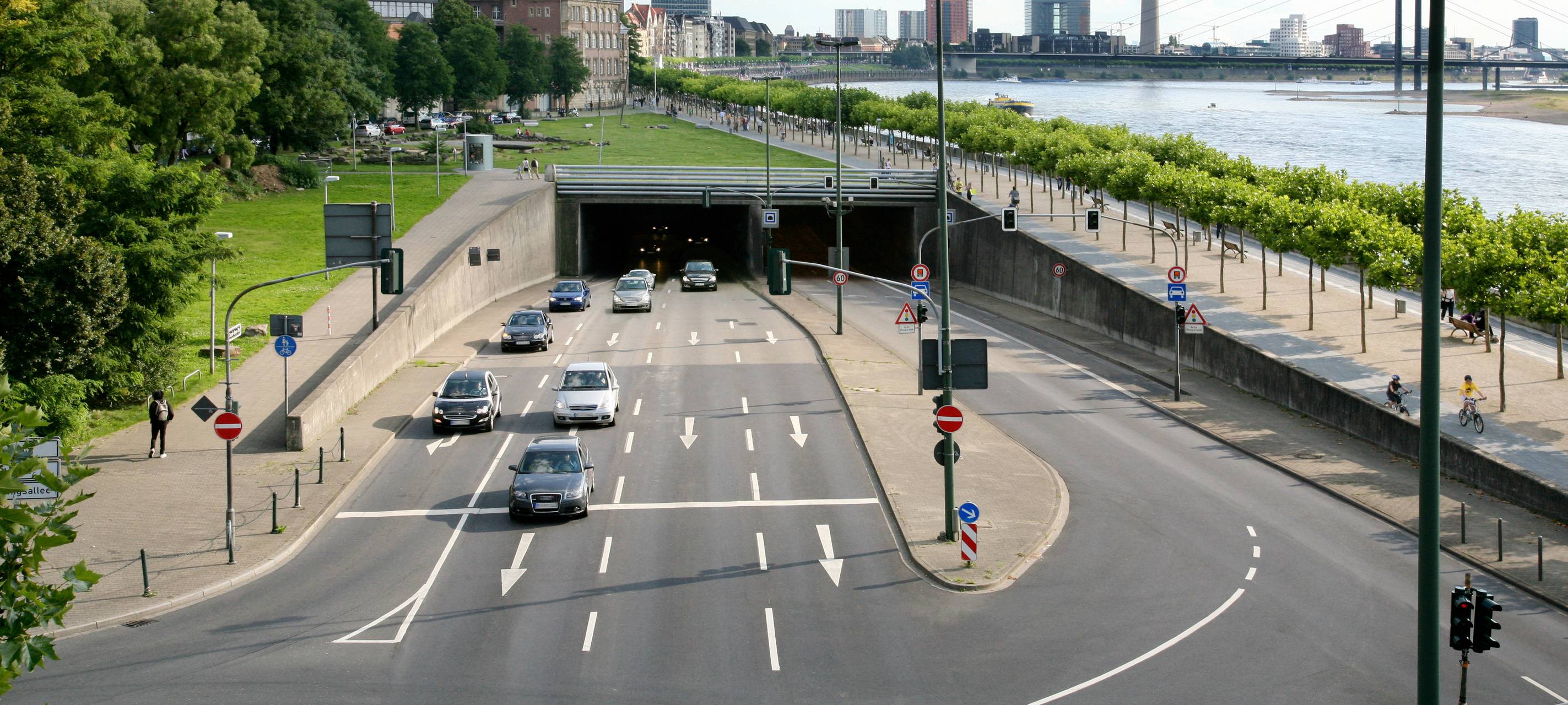 Der Rheinufertunnel und Autos. Hinter der Ausfahrt in Richtung Norden ist St. Lambertus, der Rheinturm und der Rhein erkennbar.