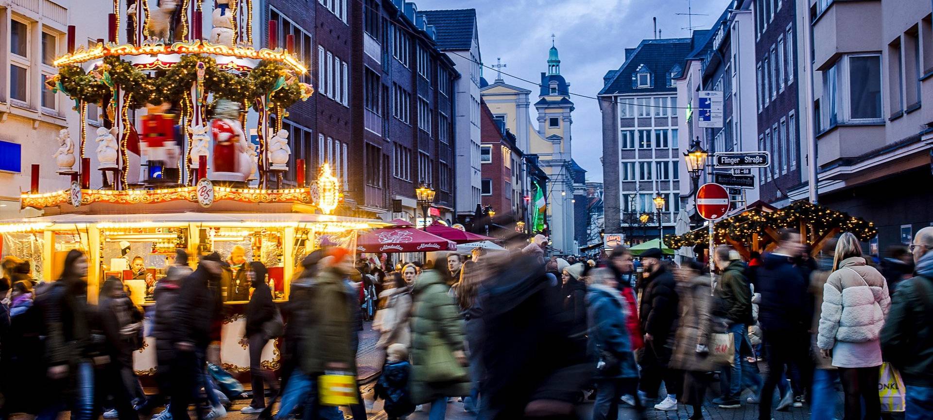 Weihnachtsmärke Überblick: Weihnachtsmarkt auf der Flingerstraße in der Altstadt. Viele Menschen sind unterwegs. Im Hintergrund ist die Andreaskirche erkennbar.