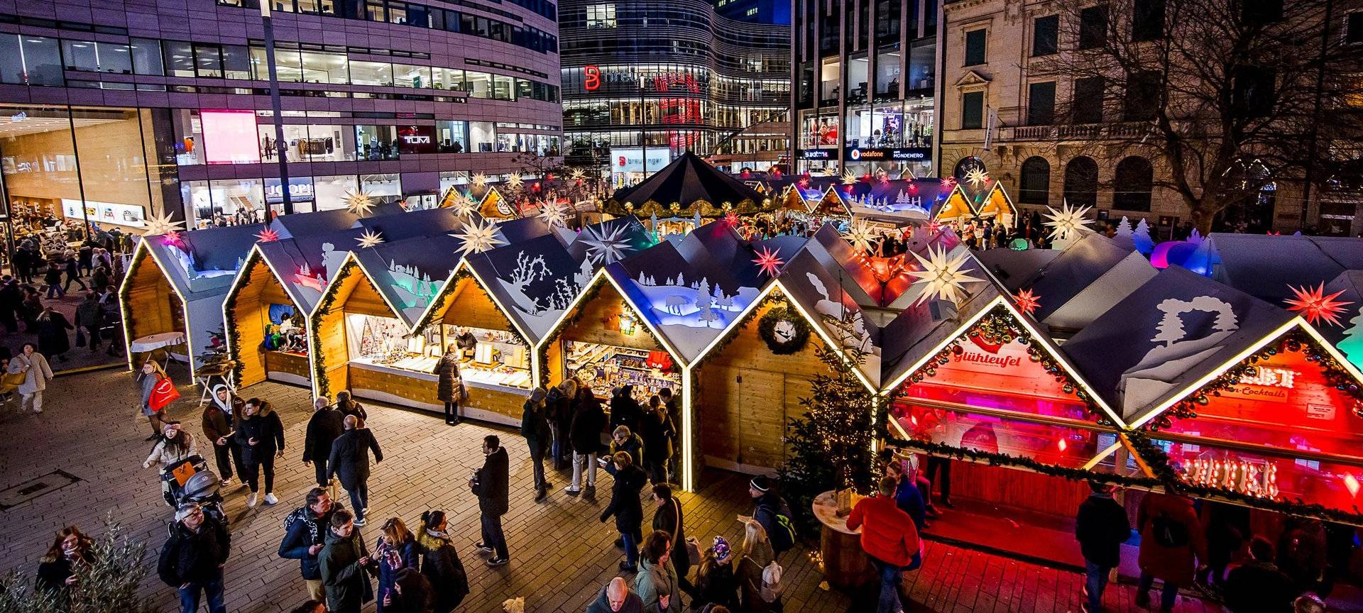 Weihnachtsmärke Überblick: Der Weihnachtsmarkt auf dem Schadowplatz. Mit vielen bunten Buden. Im Hintergrund ist der Kö-Bogen II zu erkennen.