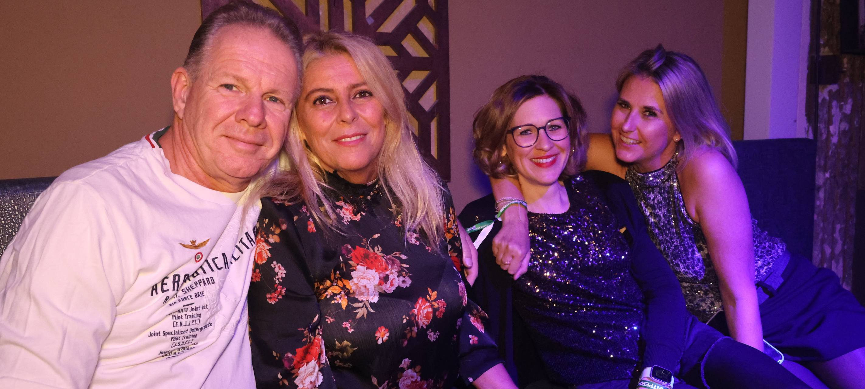 Ein Mann posiert mit einer Dame für ein Foto. Daneben liegen sich noch zwei weitere Damen in den Armen.