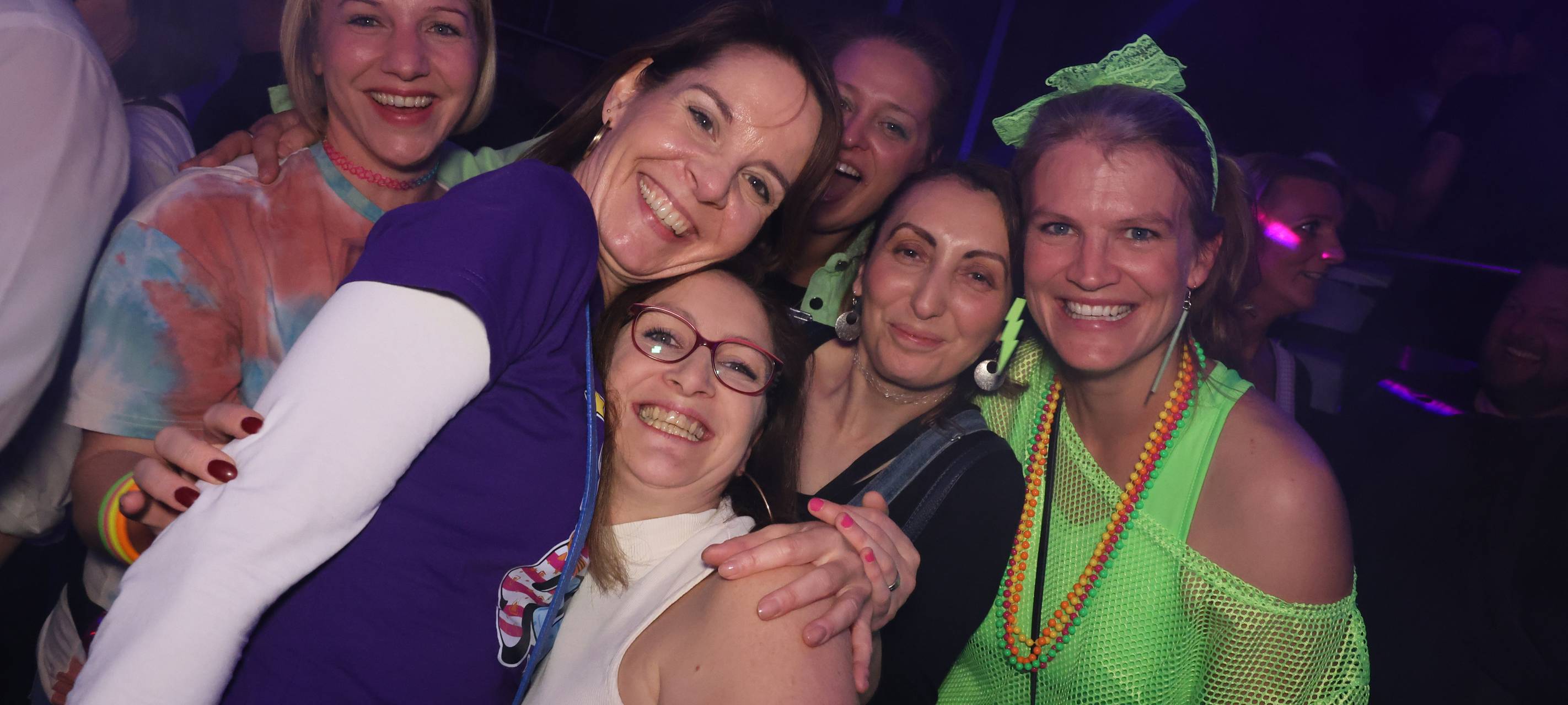 90er-Party: Vier Damen machen ein gemeinsames Gruppenfoto in der Nachtresidenz. Teilweise sind sie im 90er-Jahre-Stil mit Neonfarben gekleidet. Sie lachen und sehen glücklich aus.