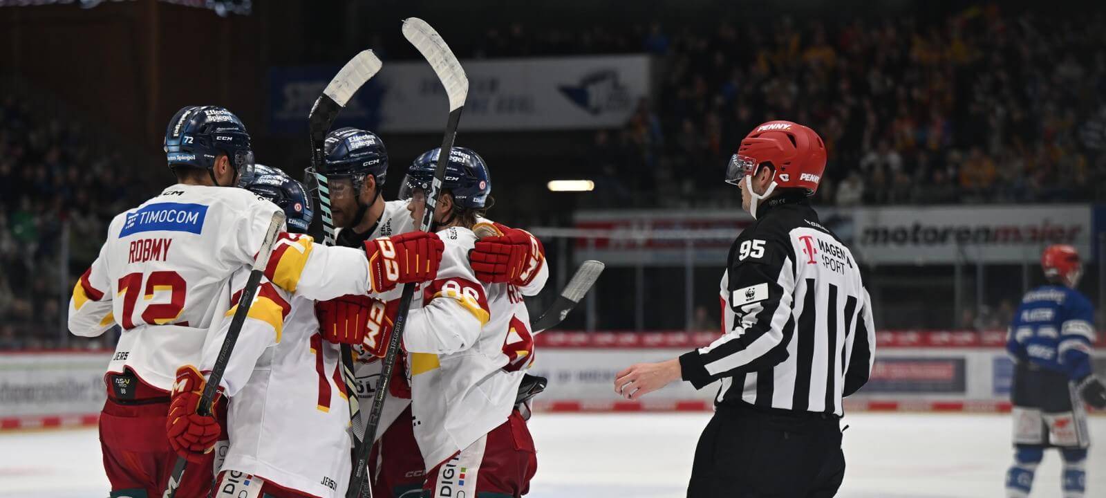 Im Vordergrund feiern einige Spieler der DEG auf dem Eis und umarmen sich. Daneben steht ein Schiedsrichter. Im Hintergrund sind ein Gegenspieler und die Ränge des Eisstadions zu sehen.