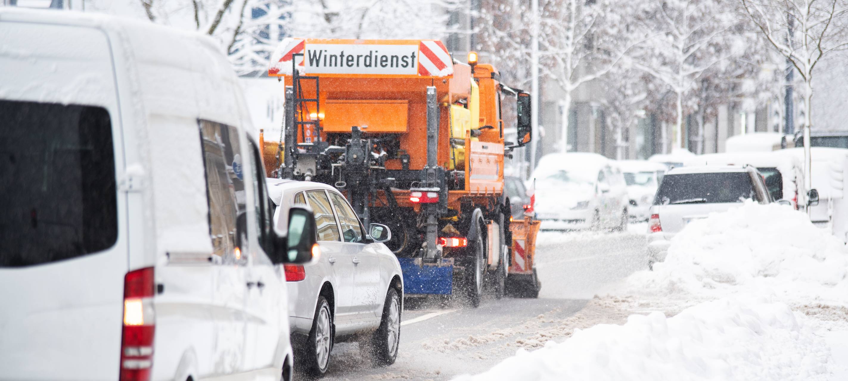 Ein Winterdienst-Fahrzeug im Einsatz. Hinter dem Streufahrtzeug fahren langsam weitere Autos.