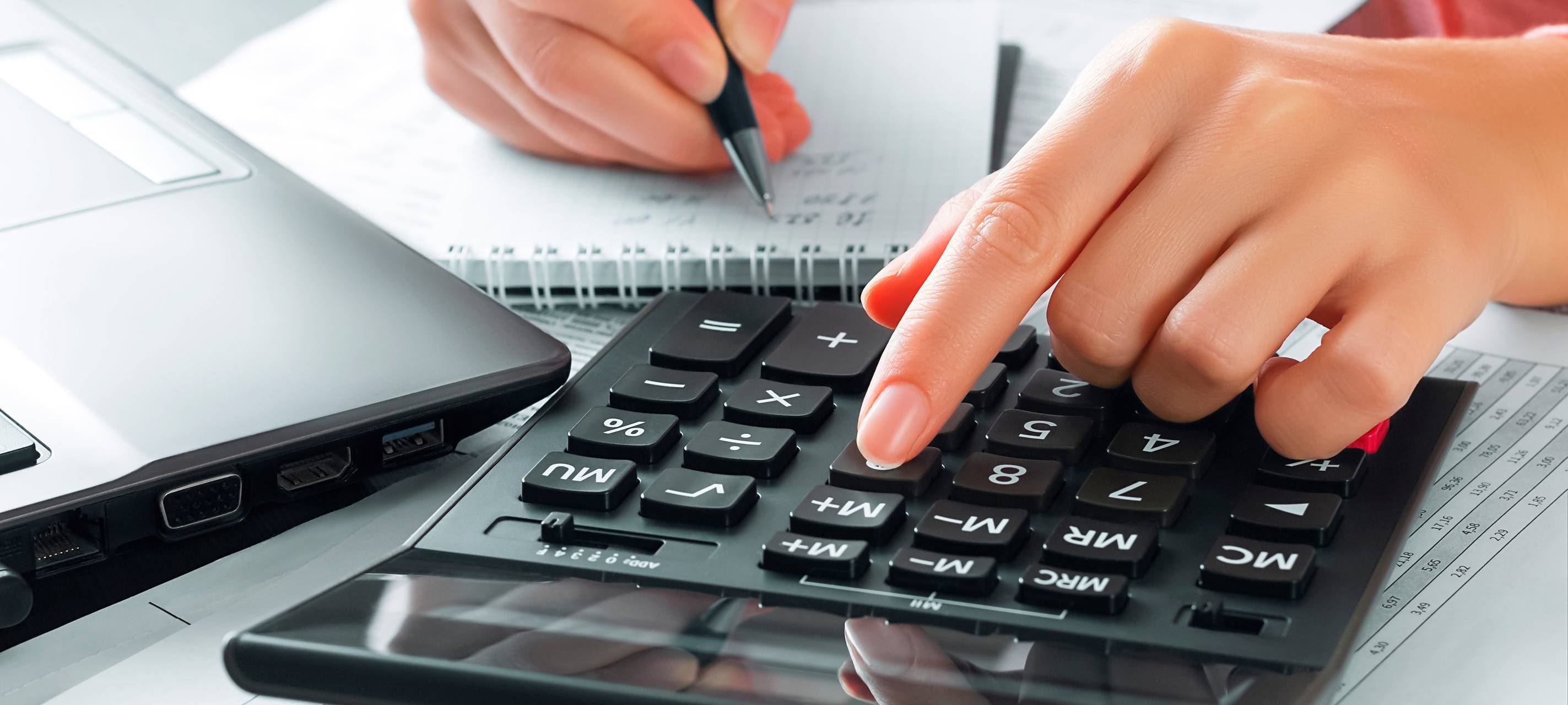 Eine Buchhalterin im Büro benutzt einen Taschenrechner und schreibt Daten in ein Notizbuch.