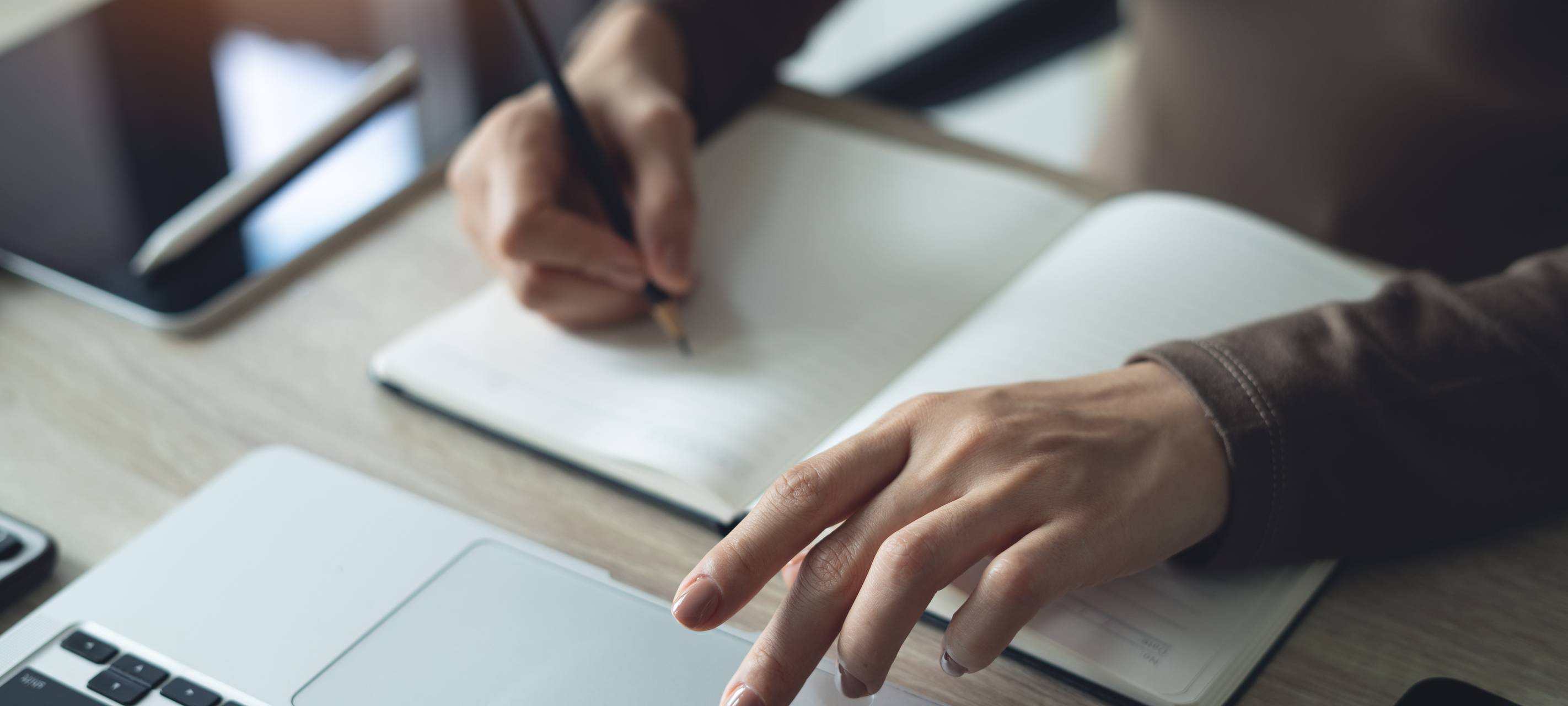 Nahaufnahme: Eine Geschäftsfrau nutzt einen Laptop-Computer, um Informationen zu suchen und macht Notizen in ein Notizbuch auf dem Bürotisch.