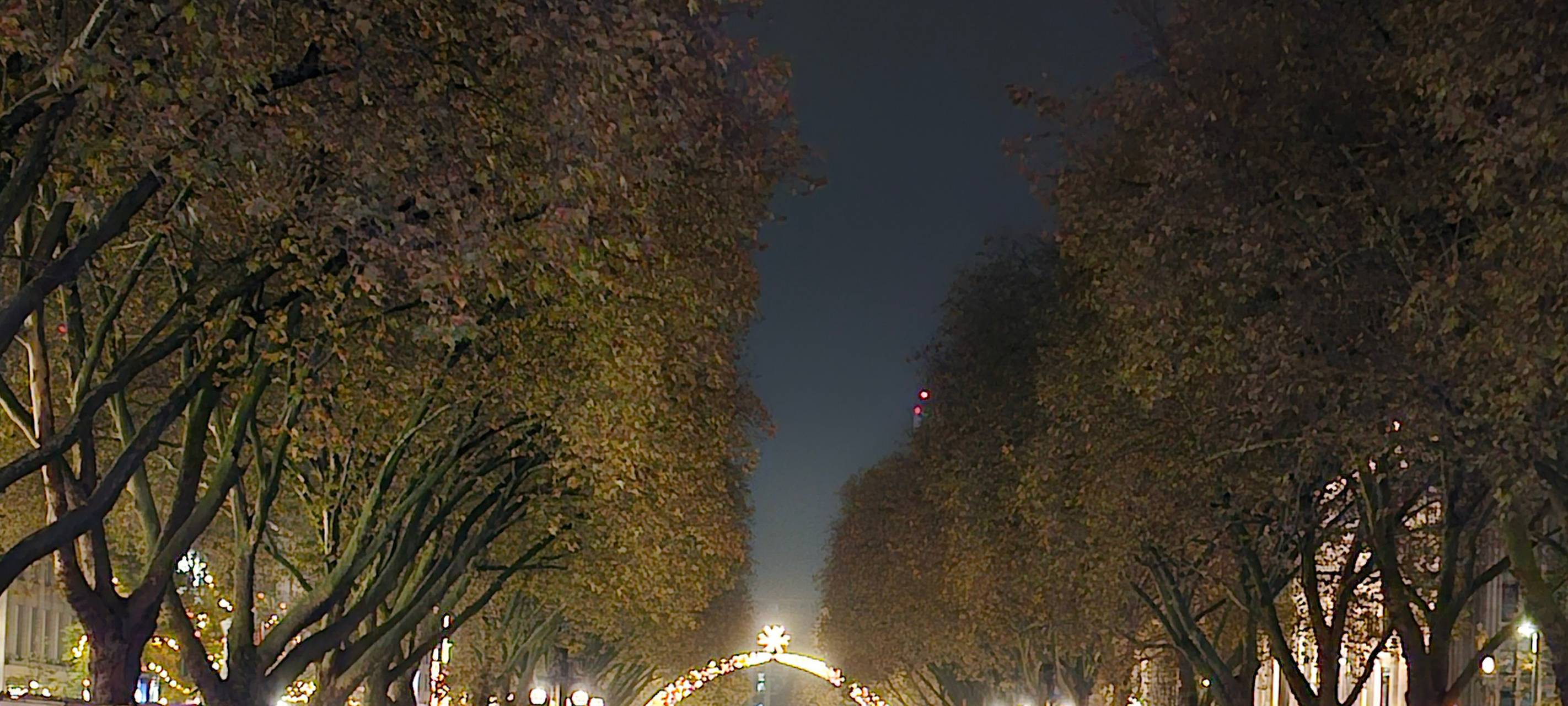 Die Königsallee mit dem Kö-Graben bei Nacht. Im Hintergrund leuchtet der Lichterdom auf der Steinstraße.