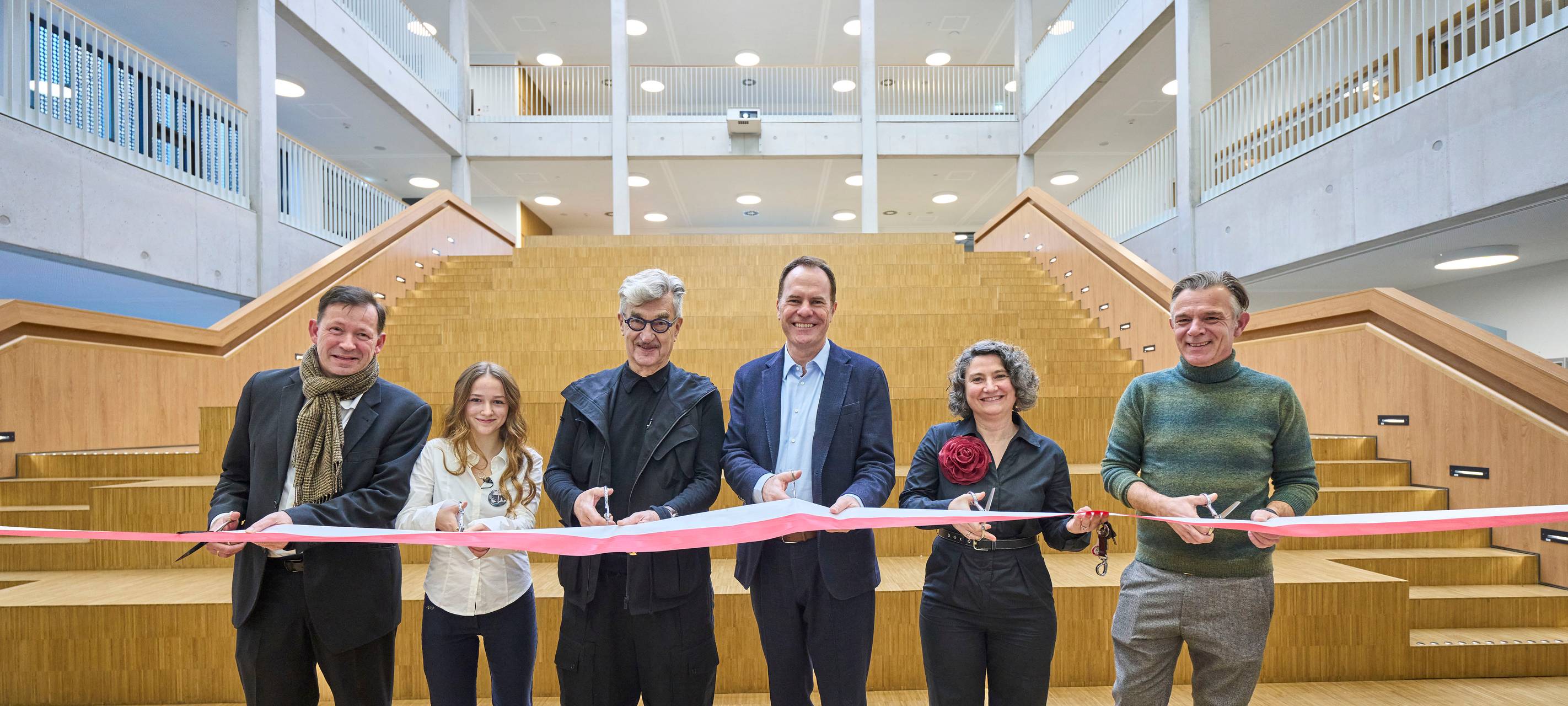 Wim Wenders zerschneidet zur Einweihung des Wim-Wenders-Gymnasiums feierlich ein Band. Auch Oberbürgermeister Stephan Keller legt Hand an.