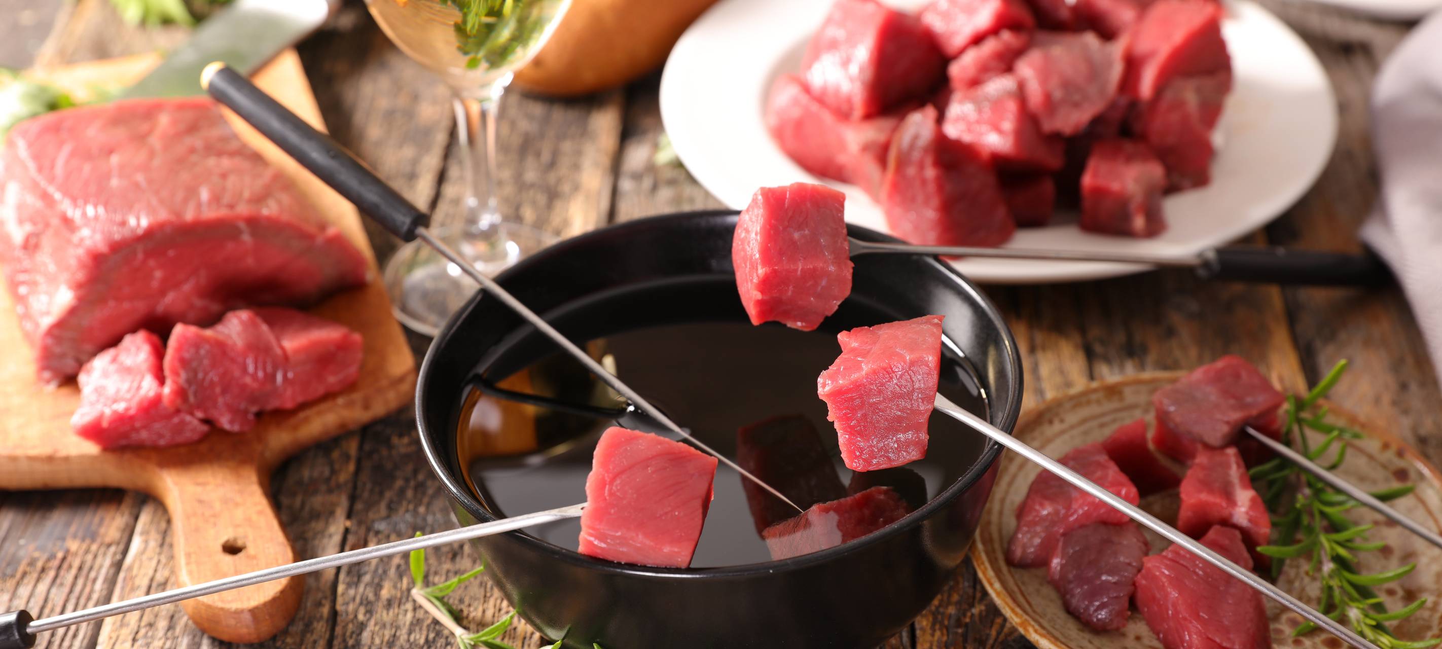 Ein Fondue-Topf mit Fleisch und einem Glas Weiswein.
