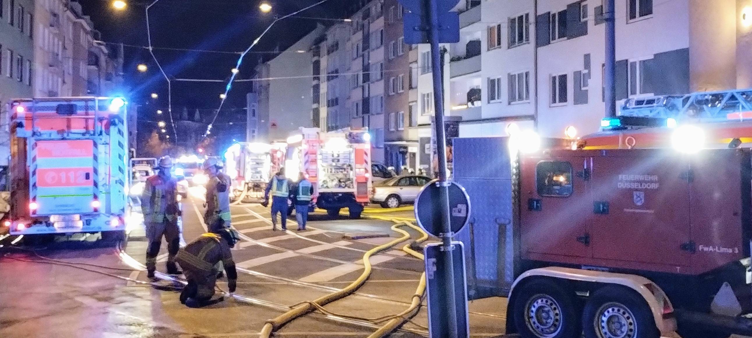 Eine Straße in Düsseldorf im dunkeln. Einsatzfahrzeuge der Feuerwehr stehen mit Blaulicht auf der Straße. Es sind auch Einsatzkräfte von Feuerwehr und Polizei zu sehen.