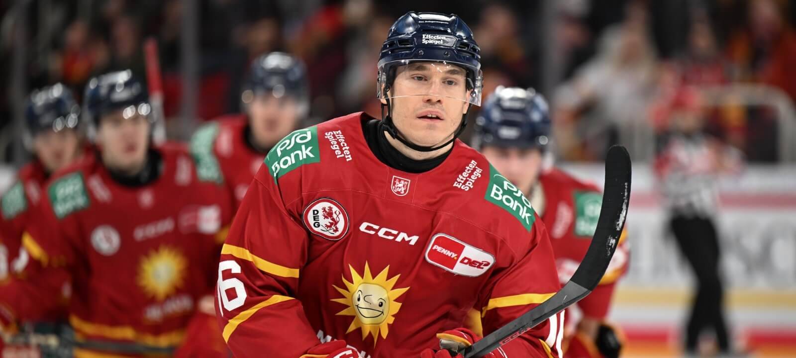 Im Vordergrund läuft DEG-Verteidiger Kyle Cumiskey über das Eis. Im Hintergrund sind unscharf einige weitere Mitspieler zu sehen.