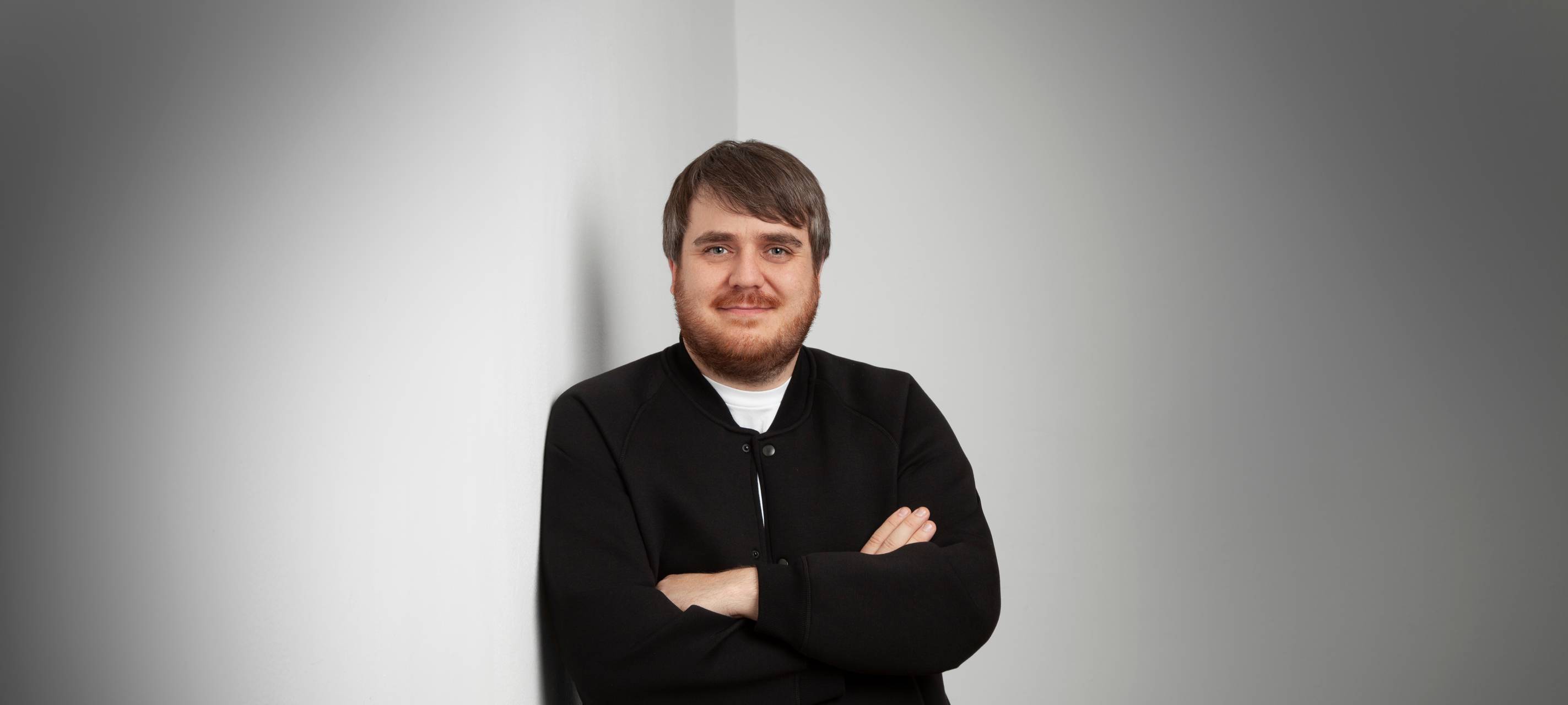 Der neue Gastro-Beauftragte der Stadt DüsseldorfJörn Topel posiert vor einer weißen Wand. Er trägt eine schwarze Hemd-Jacke und ein weißes T-Shirt und hat die Arme verschränkt