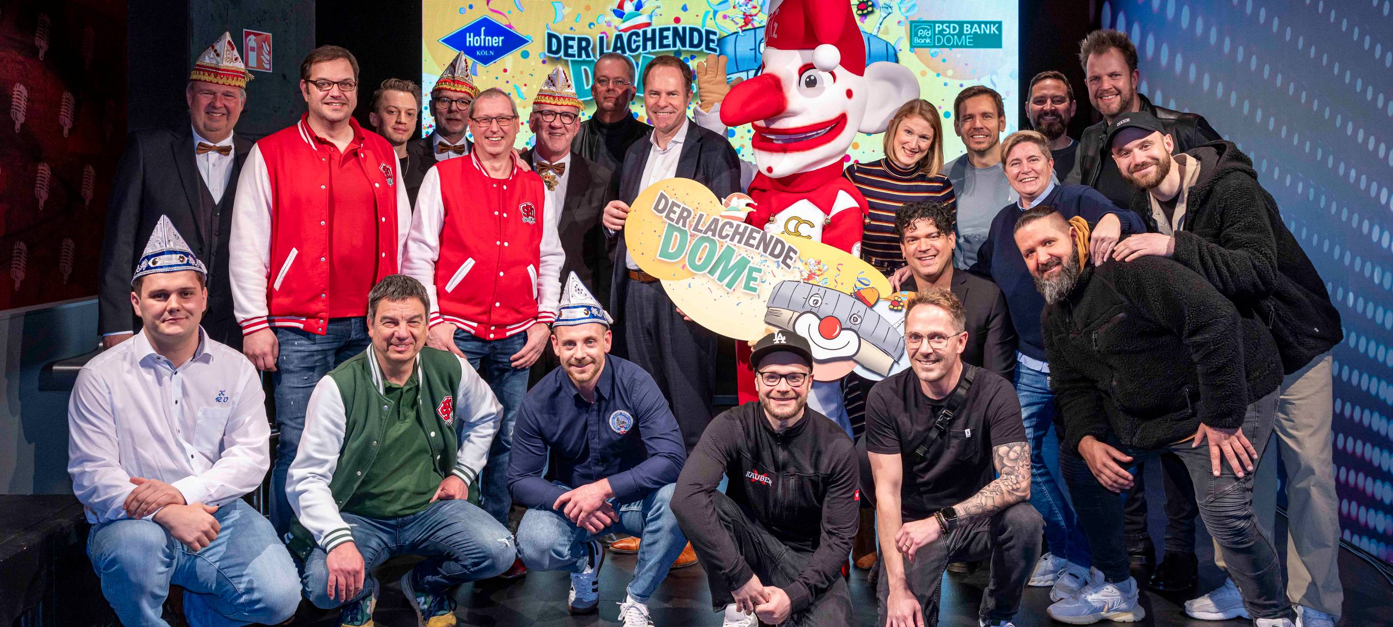 Eine Gruppe von Düsseldorfer Karnevalisten stehen vor einem Schild mit der Aufschrift "Der lachende DOME". In der Mitte ist Oberbürgermeister Stephan Keller zu sehen.