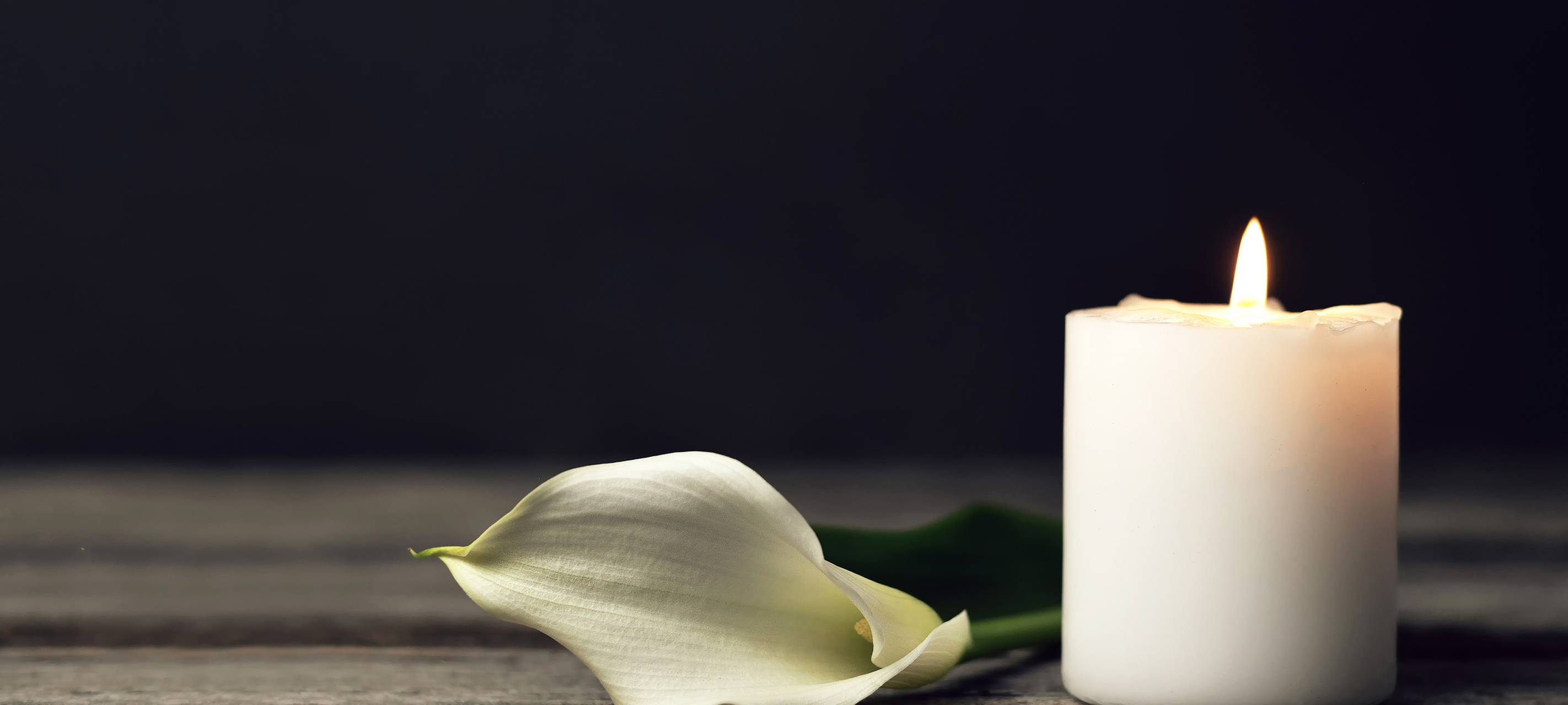 Brennende Kerze und weiße Calla-Lilie auf dunklem Hintergrund.