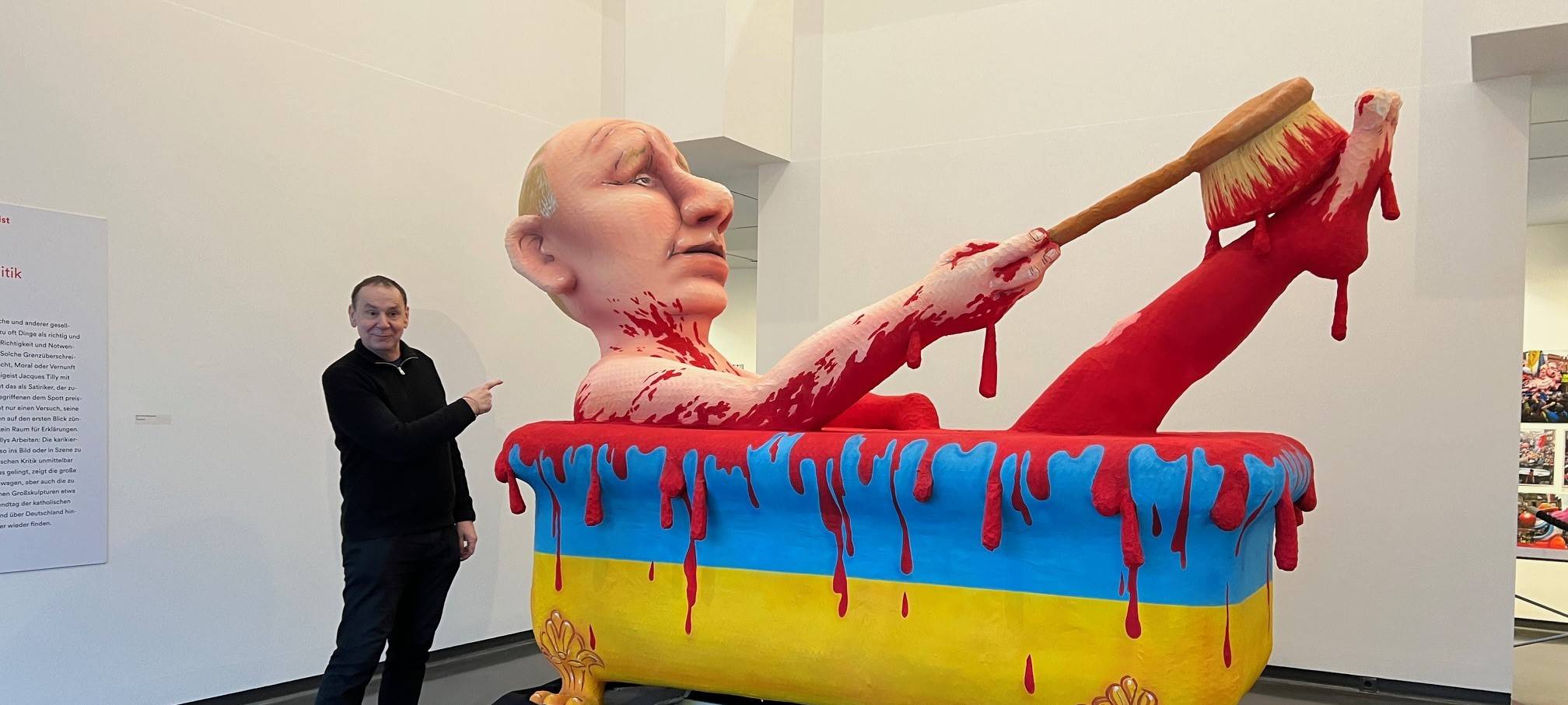 Putin badet in Blut, die Badewanne ist die Ukraine. Davor steht Jacques Tilly