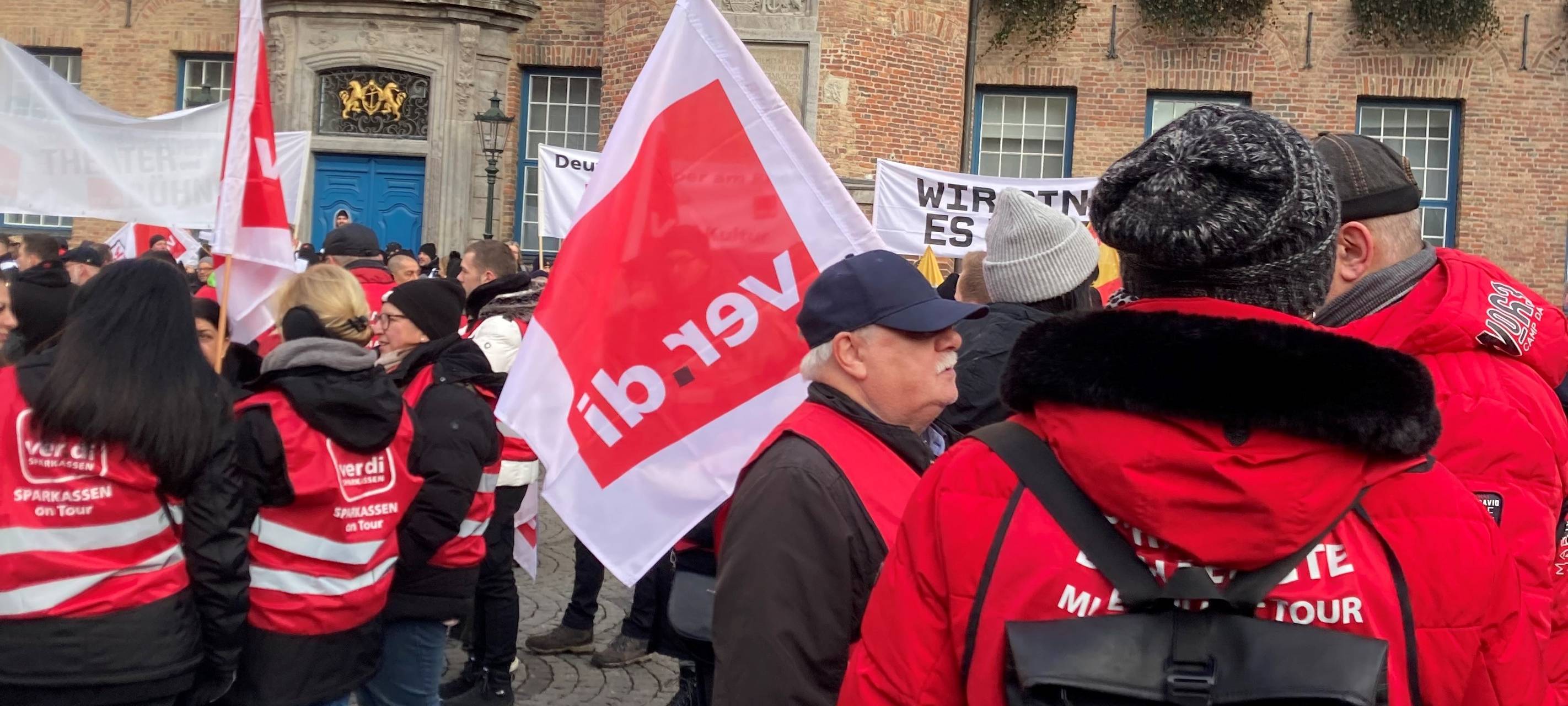 Streikende Menschen vor dem Düsseldorfer Rathaus. Sie tragen Fahnen und rote Warnwesten.