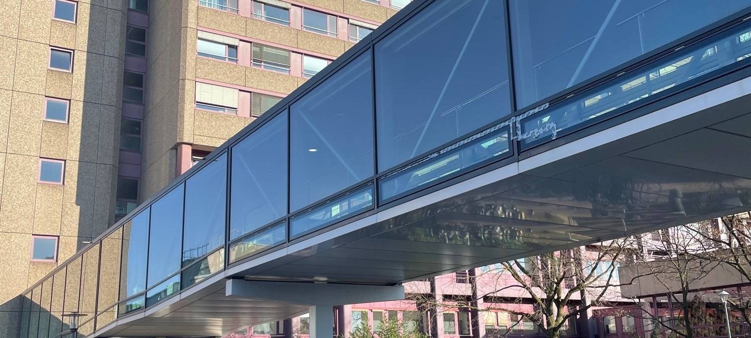 Eine gläserne Brücke auf dem Campus der Uni-Klinik unter der mehrere Polizeiautos stehen. Die Brücke führt zu einem Hochhaus.