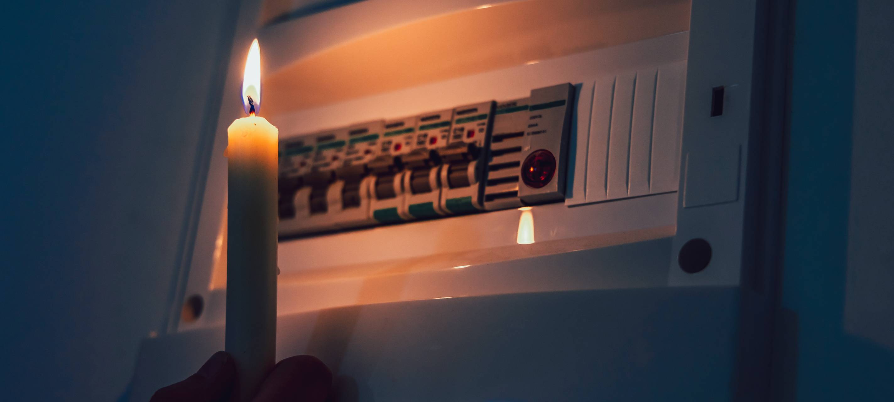 Ein Sicherungskasten während eines Stromausfalls. Der Kasten wird von einer brennenden Kerze beleuchtet.
