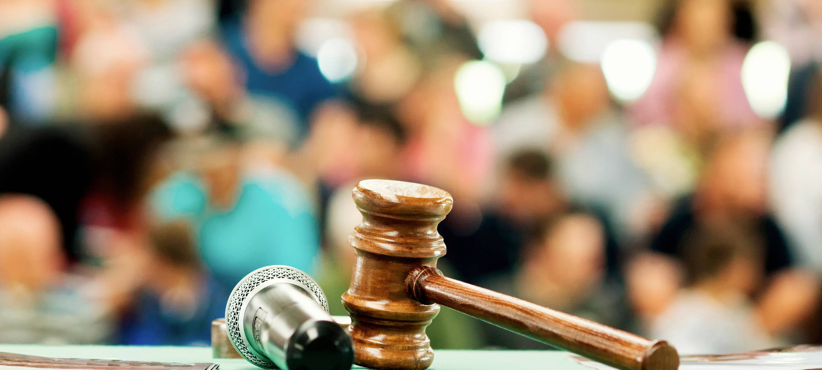 Eine Szene aus einer Versteigerung, bzw. Auktion. Ein Auktionshammer und ein Mikro liegen vor einer Menschengruppe.