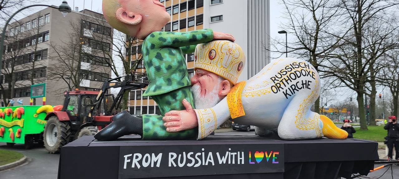 Mottowagen beim Karneval: Die russische-orthodoxe Kirche kniet vor Putins Schritt, der ihren Kopf festhält.