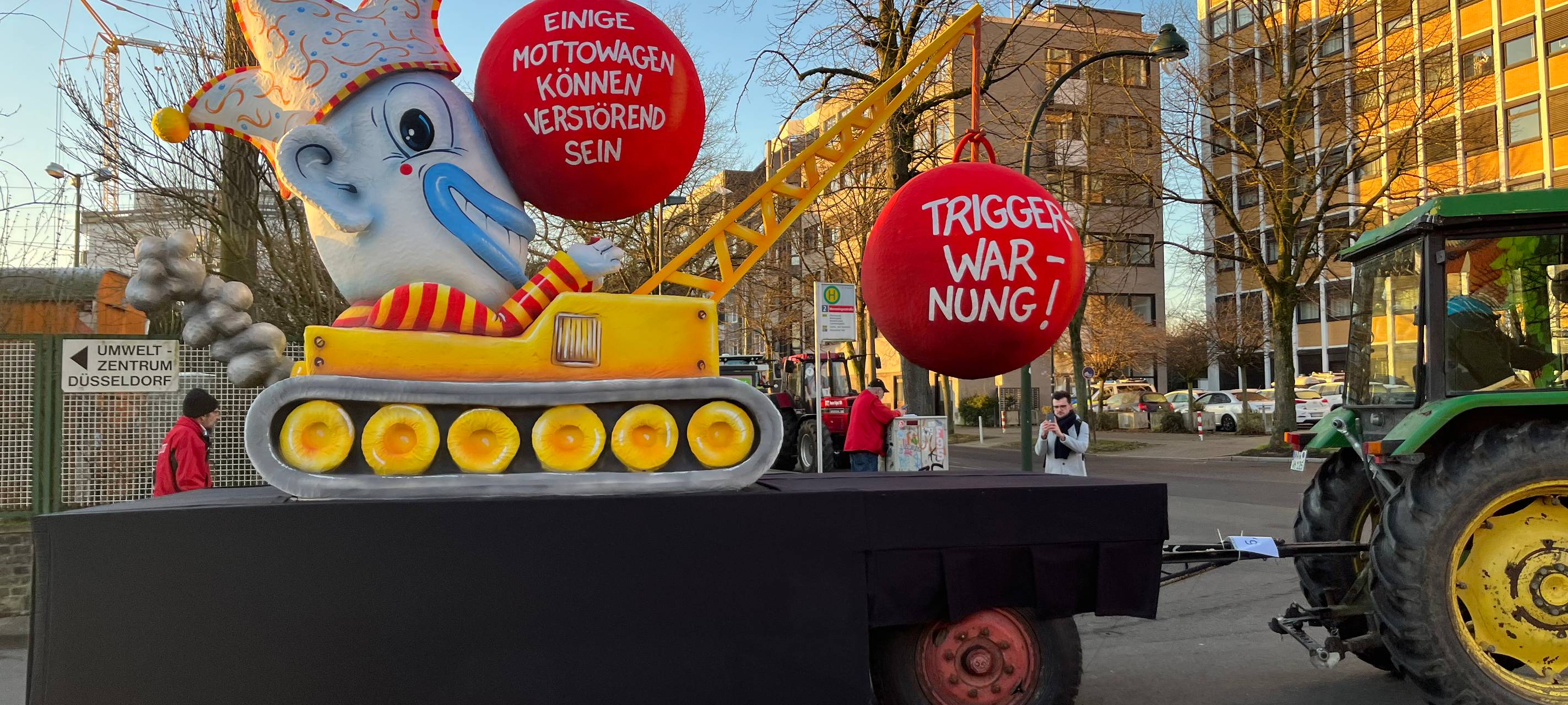 Mottowagen beim Karneval: Der Karneval als Abrissbirne im Clownskostüm, die Kugel als Triggerwarnung.