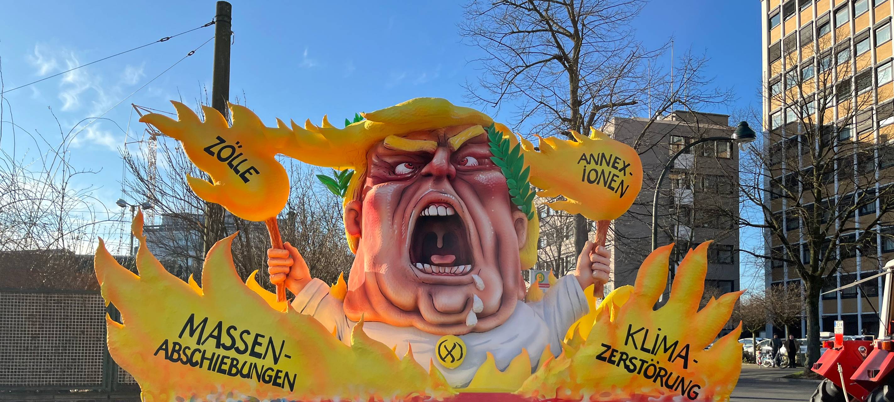 Mottowagen beim Karneval: Trump schreiend zwischen Flammen und hält selbst die Fackeln in der Hand