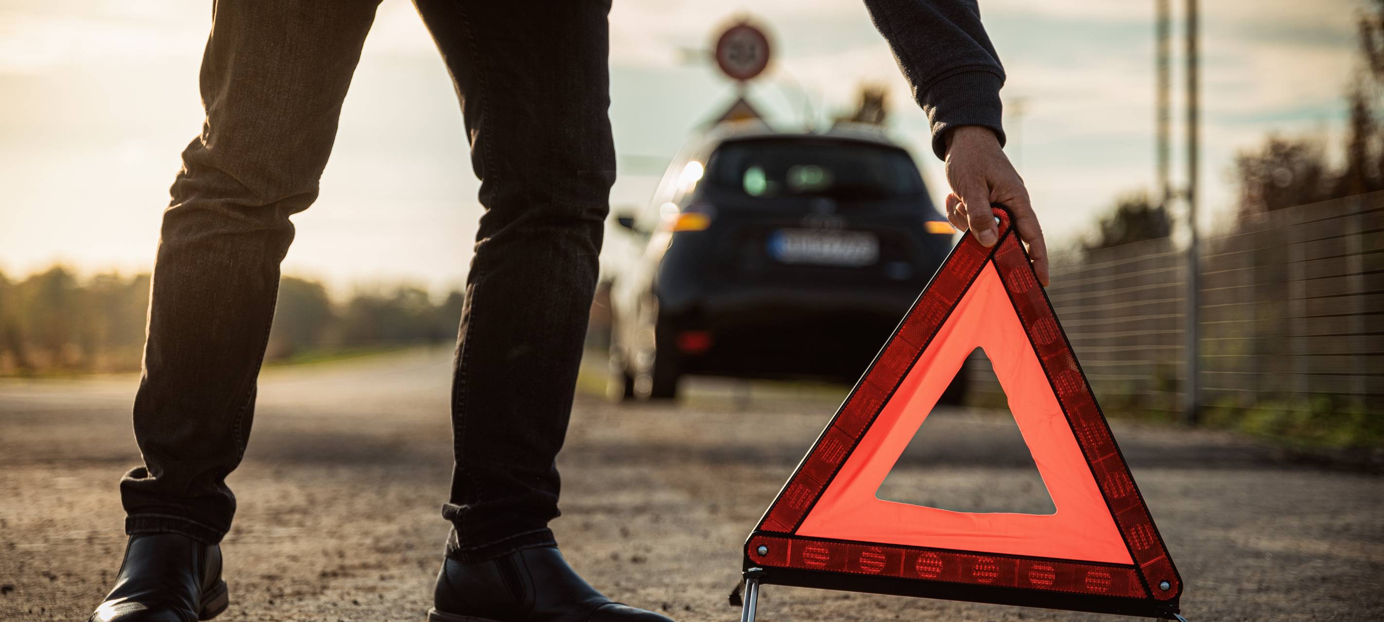 Ein Autofahrer mit Autopanne stellt ein Warndreieck auf.