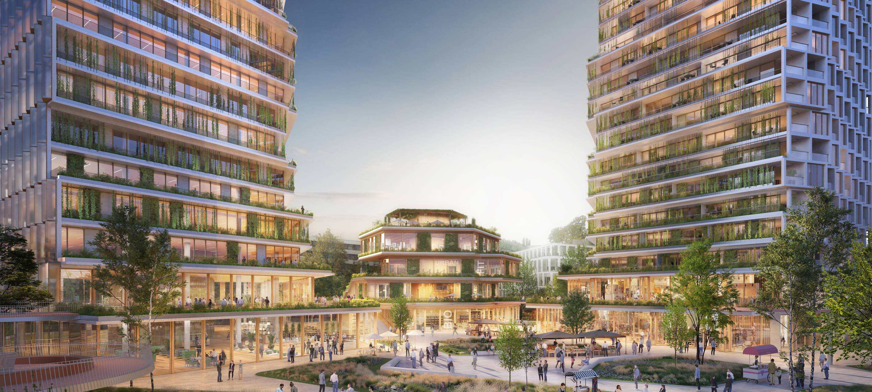 Zwei nebeneinander stehende, begrünte Hochhäuser. In der Mitte steht auf einer beleuchteten Plaza ein weiteres, kleineres Gebäude.