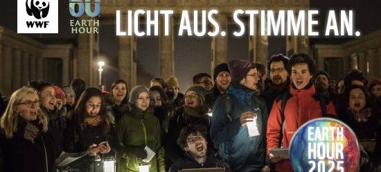 Viele Menschen stehen mit offenen Mündern weitestgehend im Dunkeln. Einige Laternen beleuchten die Szenerie zur Earth Hour 2025.