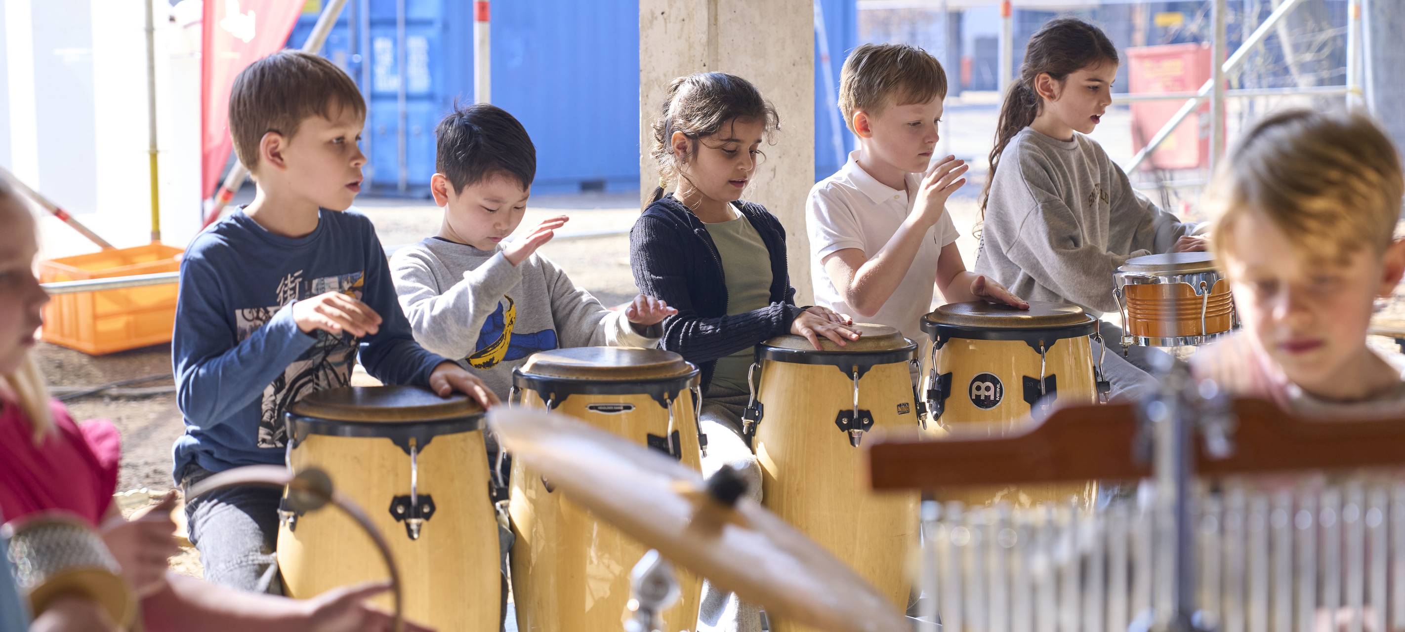 Schülerinnen und Schüler der Rolandschule mit Trommeln und anderen Musikinstrumenten. Die Kinder spielen zum Richtfest für den Erweiterungsbau. Im Hintergründ sind Baugerüste zu sehen.
