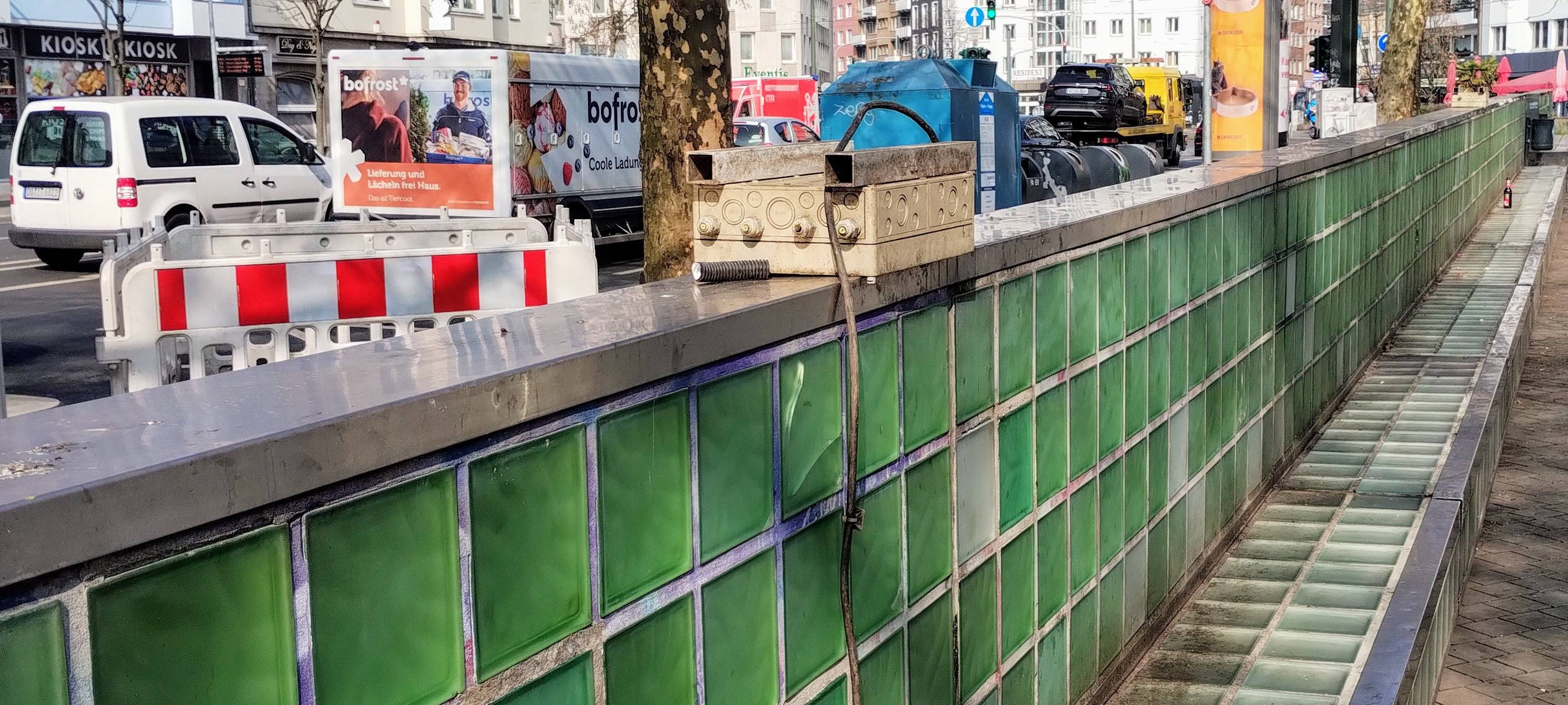 Die grünen Glasbausteine am Worringer Platz vor ihrer Beseitigung. Ein Stromkabel liegt auf der Glasbank. Im Hintergrund fließt der Verkehr.