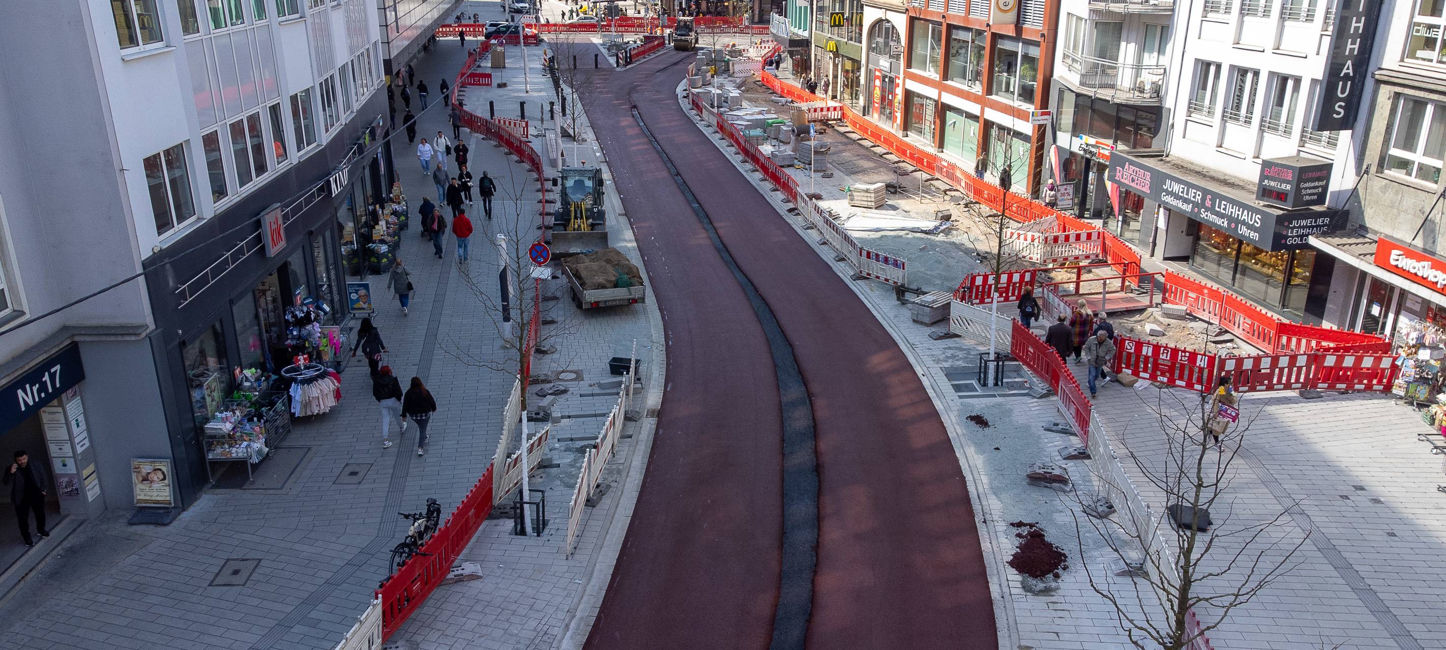 Zwei rot markierte Radspuren zwischen dem Wehrhahn und der Schadowstraße. Die unfertigen Radwege führen durch eine Baustelle, links und rechts sind Absperrungen zu sehen. Dahinter befinden sich Geschäftshäuser auf der linken und rechten Straßenseite.