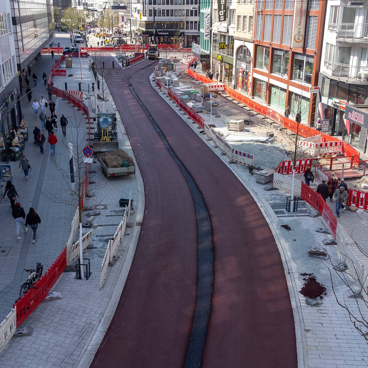 Zwei rot markierte Radspuren zwischen dem Wehrhahn und der Schadowstraße. Die unfertigen Radwege führen durch eine Baustelle, links und rechts sind Absperrungen zu sehen. Dahinter befinden sich Geschäftshäuser auf der linken und rechten Straßenseite.