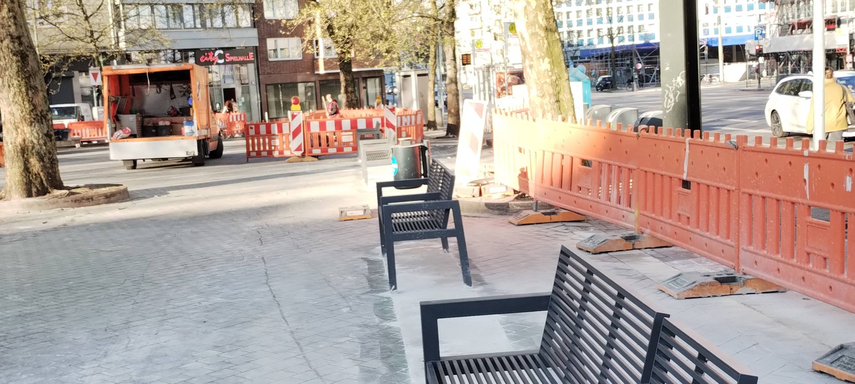 Neue, kleinere Bänke stehen auf dem Worringer Platz. Sie ersetzen die alten Glasbausteine. Im Hintergrund sind Baufahrzeuge zu sehen. Es laufen noch weitere Asphaltarbeiten.
