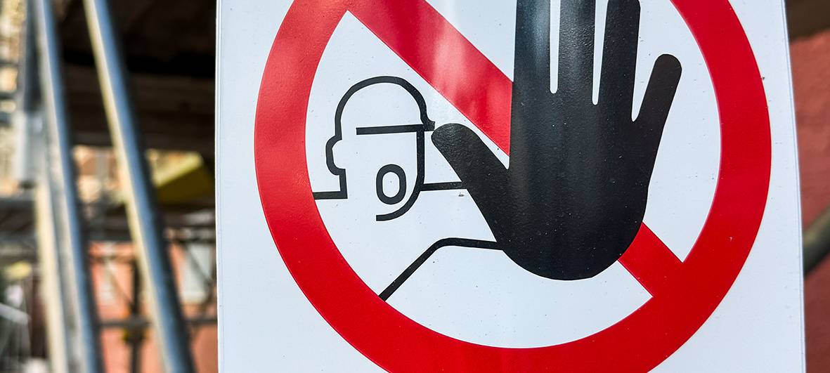 An einem Gerüst hängt ein Schild, auf dem ein durchgestrichener Roter Kreis, ein Mensch und der Schriftzug "Gerüst gesperrt" zu sehen sind.