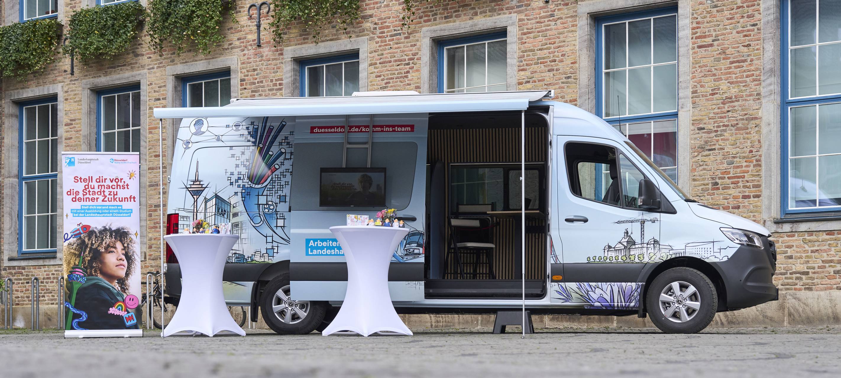 Der Karriere-Bus der Stadt steht vor dem Düsseldorfer Rathaus. Die Seitentüre ist geöffnet. Menschen können sich hier für einen Job bewerben.