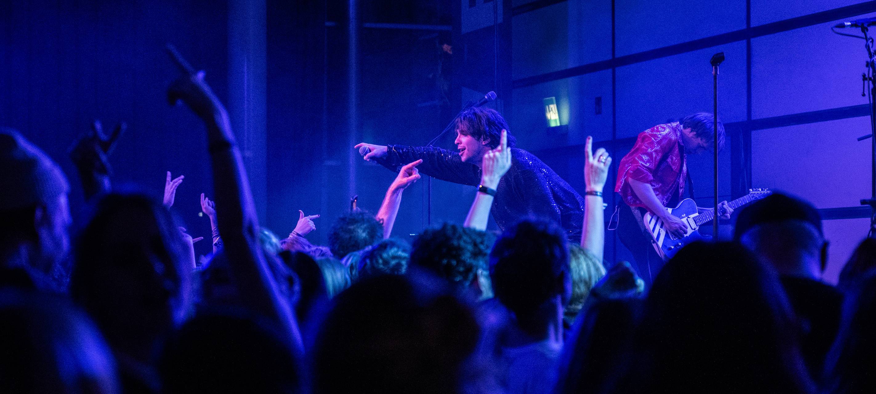 Feiernde Menschen vor einer Festival Bühne. Auf der Bühne ist der Künstler Bibiza, er streckt sein Mikrofon in die Menge.