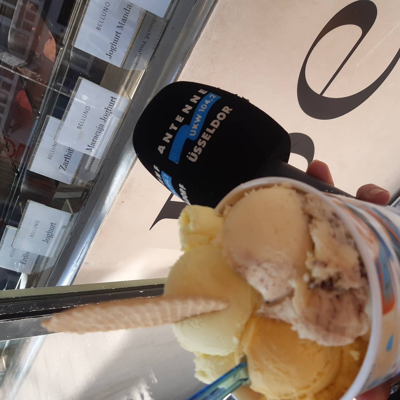 Ein Becher mit mehreren Eiskugeln, daneben das Antenne Düsseldorf Mirkofon, im Hintergrund eine Eistheke