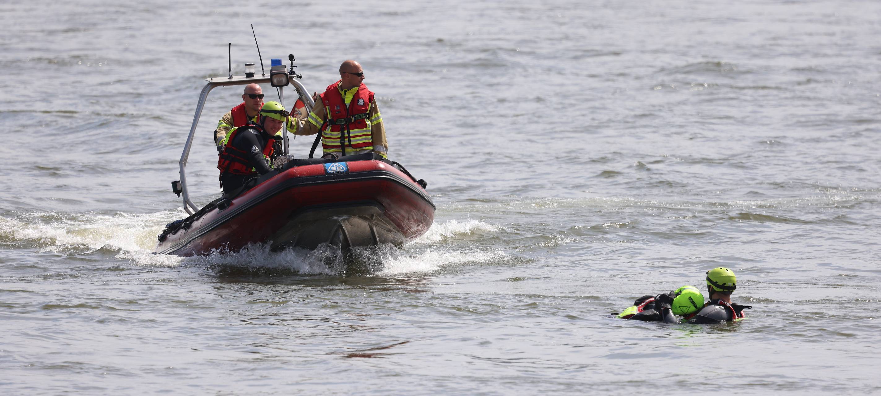 Feuerwehrboot mit Besatzung bei einer Übung auf dem Rhein. Im Wasser sind dabei ein Retter und eine zu rettende Person.